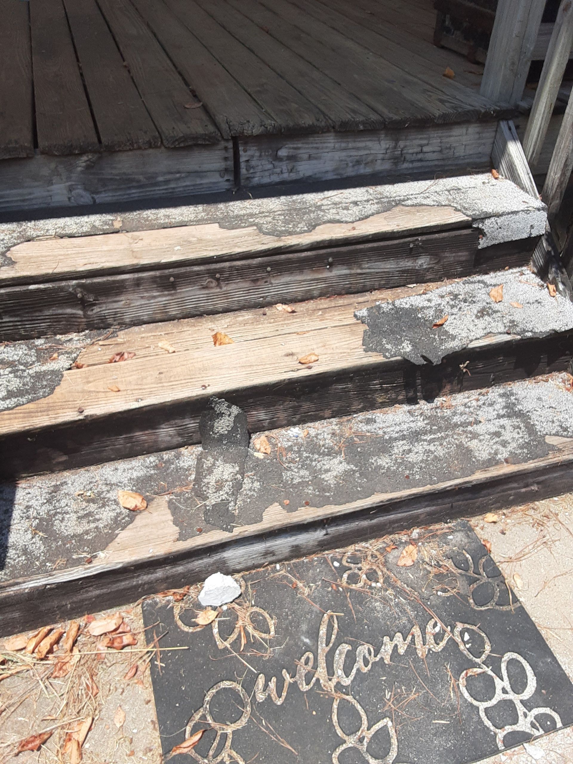A welcome mat is on the steps of a wooden porch.