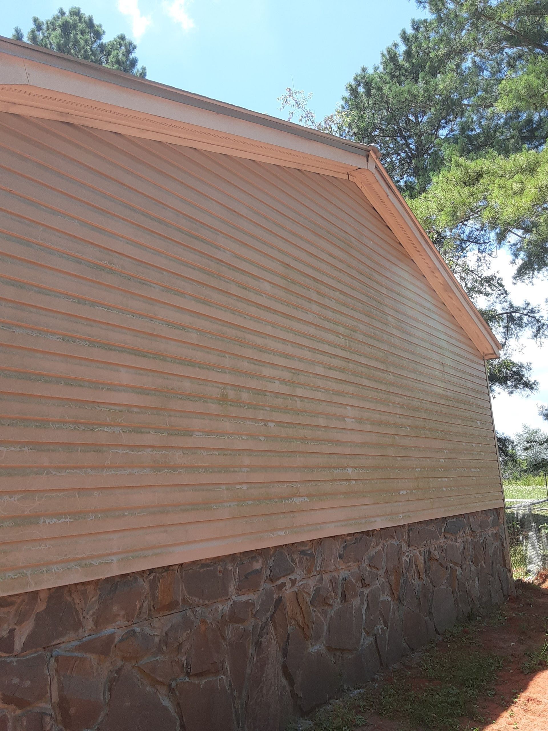The side of a house with wooden siding and a stone foundation.