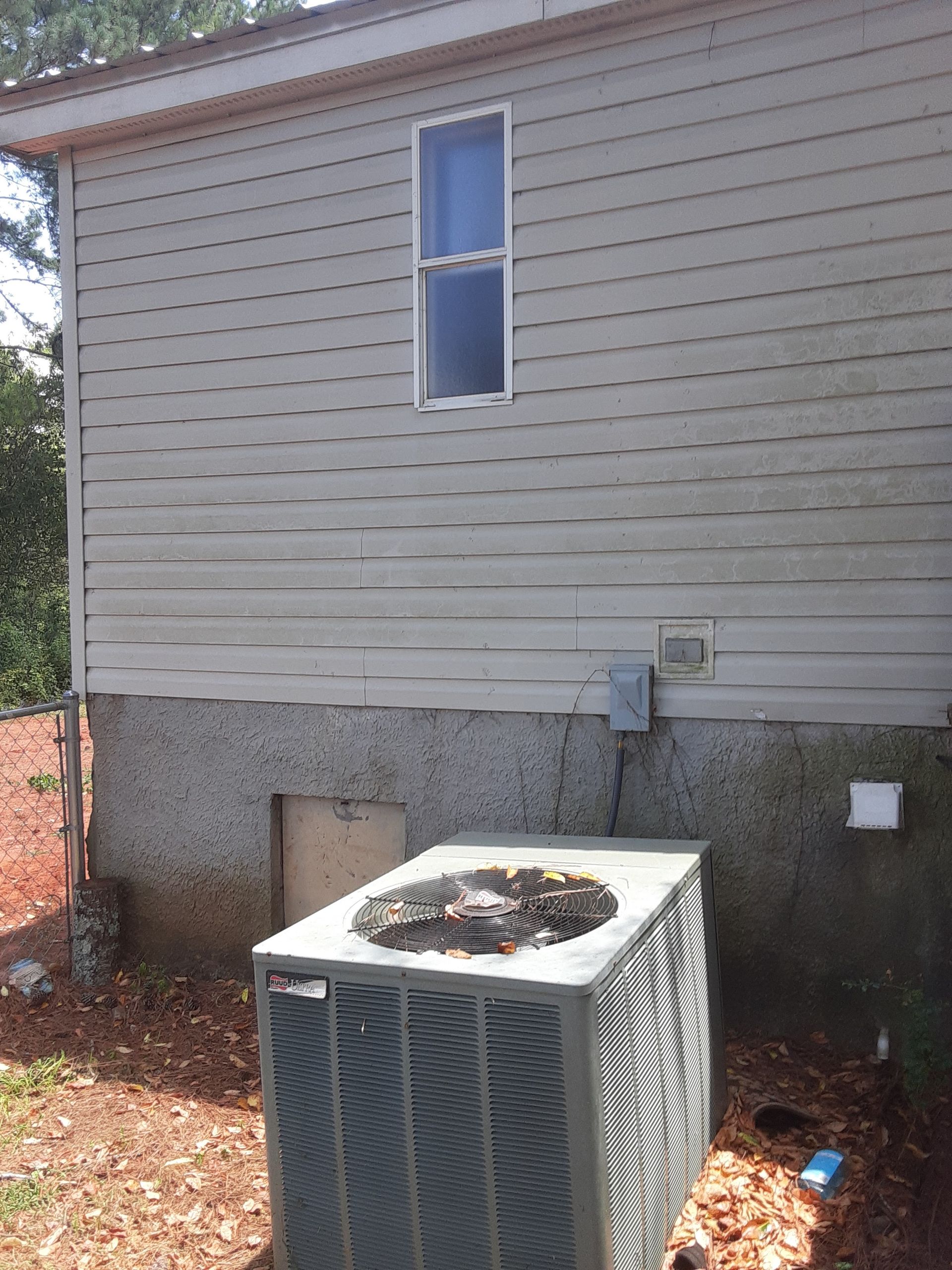 An air conditioner is sitting outside of a house next to a window.