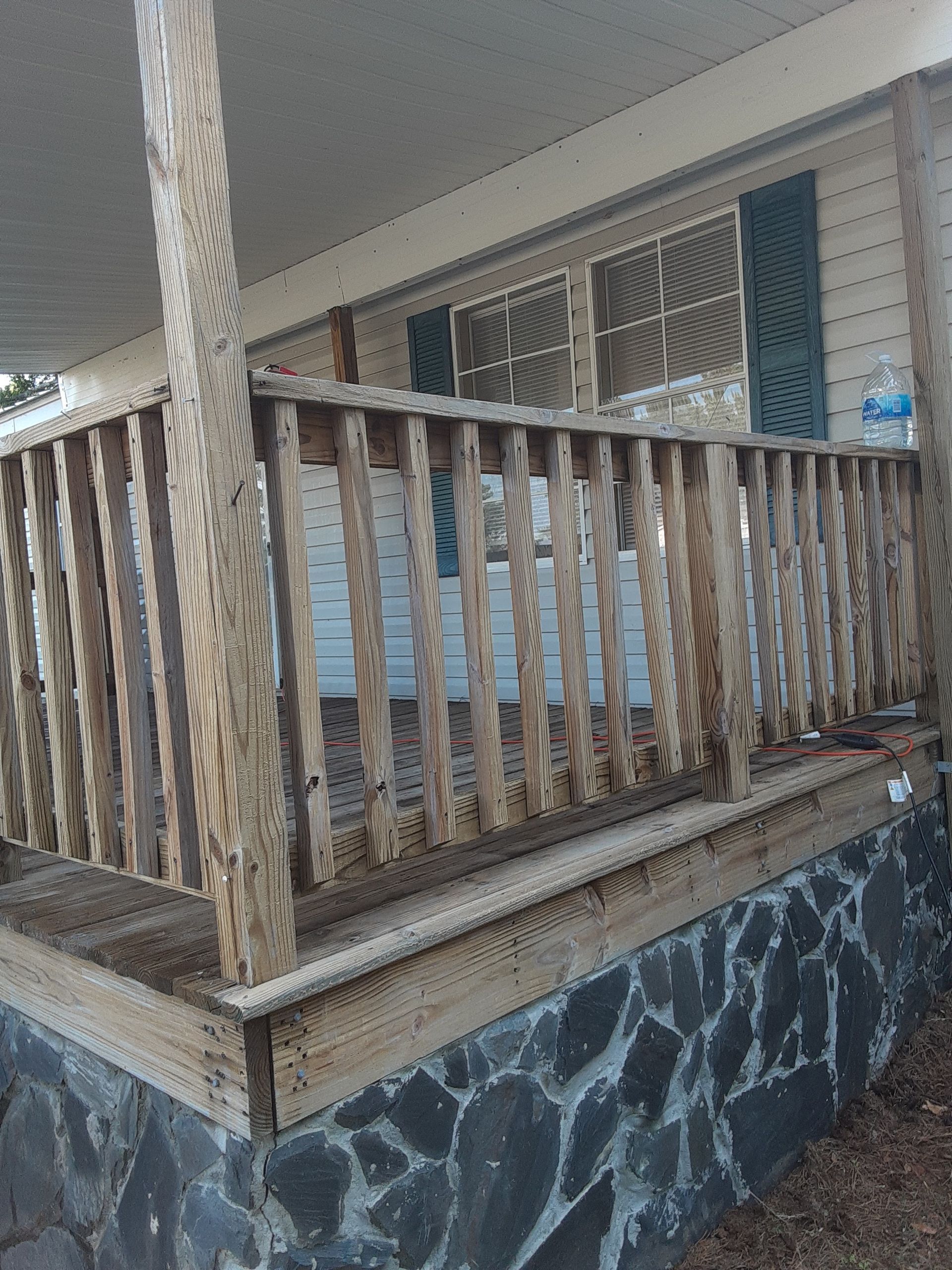 A porch with a wooden railing and a stone wall.