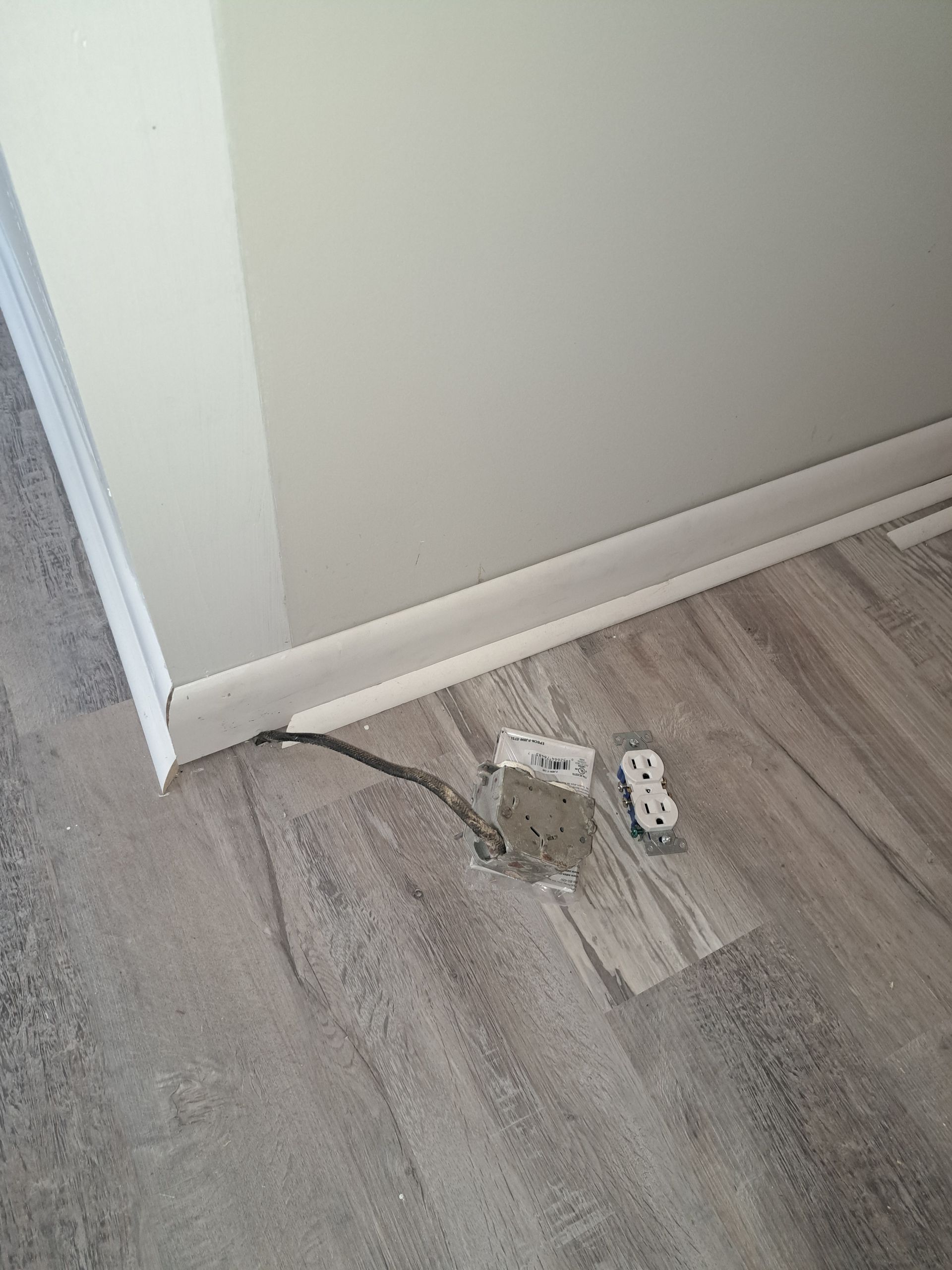 A power cord is laying on the floor next to a wall.
