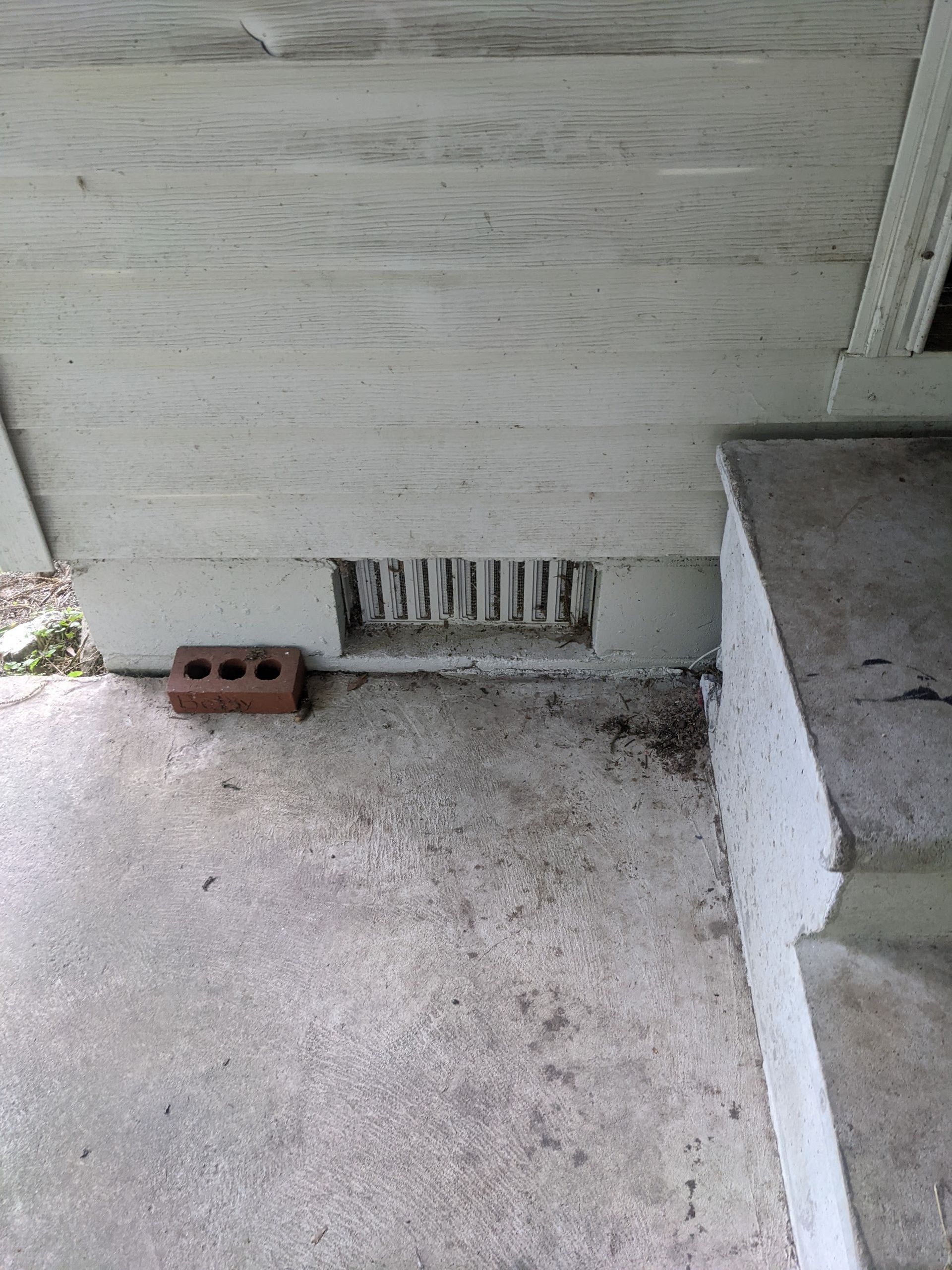 A brick is sitting on the ground next to a white wall.