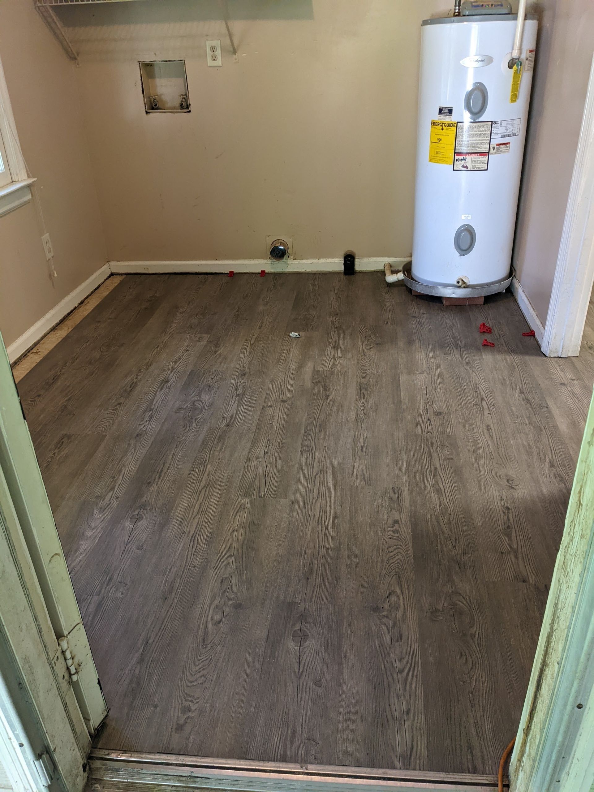 A room with a water heater and a wooden floor.