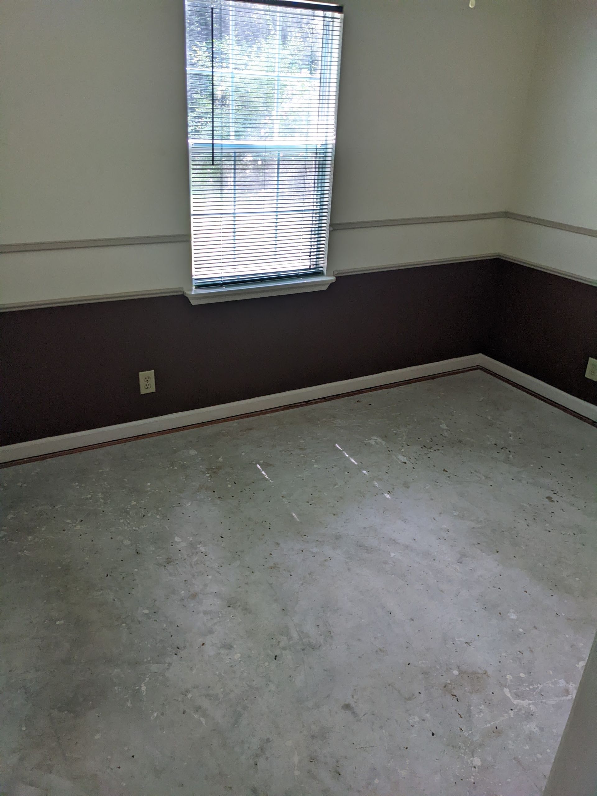 An empty room with a window and a concrete floor.