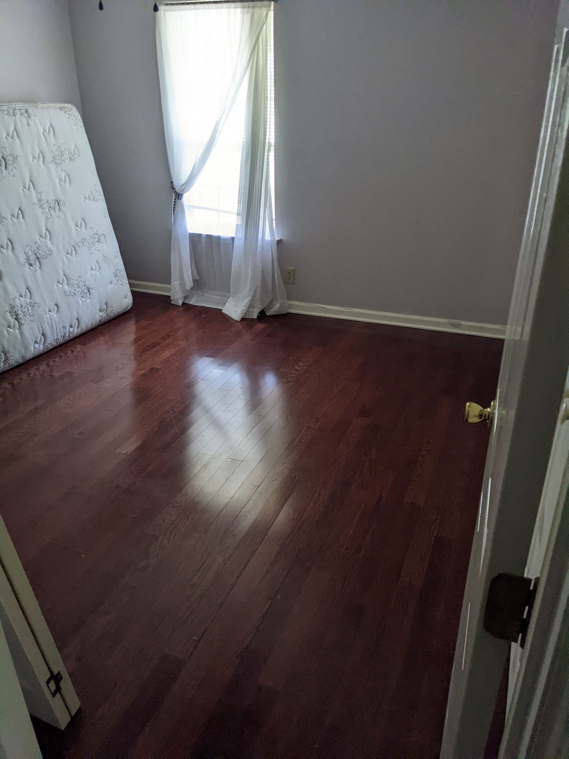A bedroom with hardwood floors , a mattress and a window.