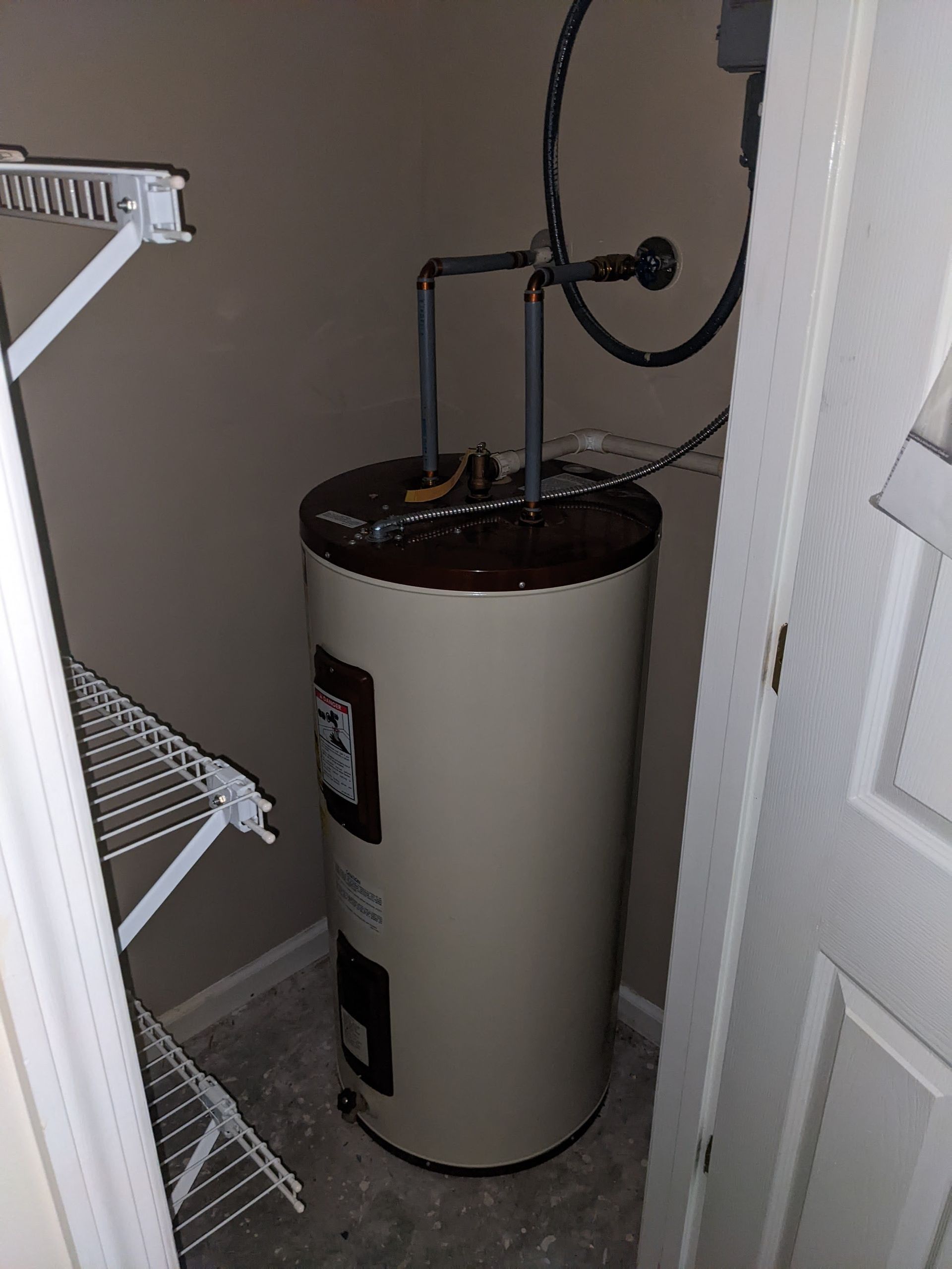 A water heater is sitting in a closet next to a door.