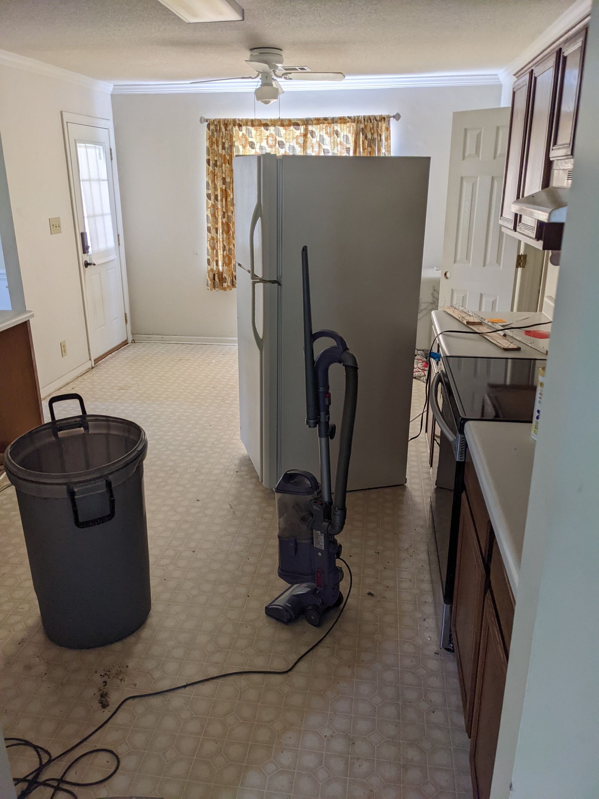 A vacuum cleaner is sitting in a kitchen next to a trash can.
