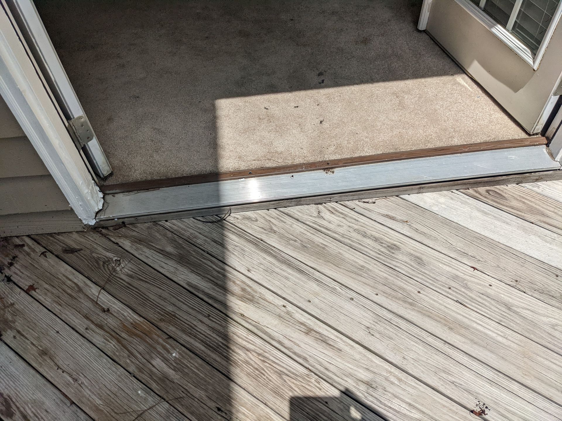 A wooden deck with a sliding glass door and a carpeted floor.