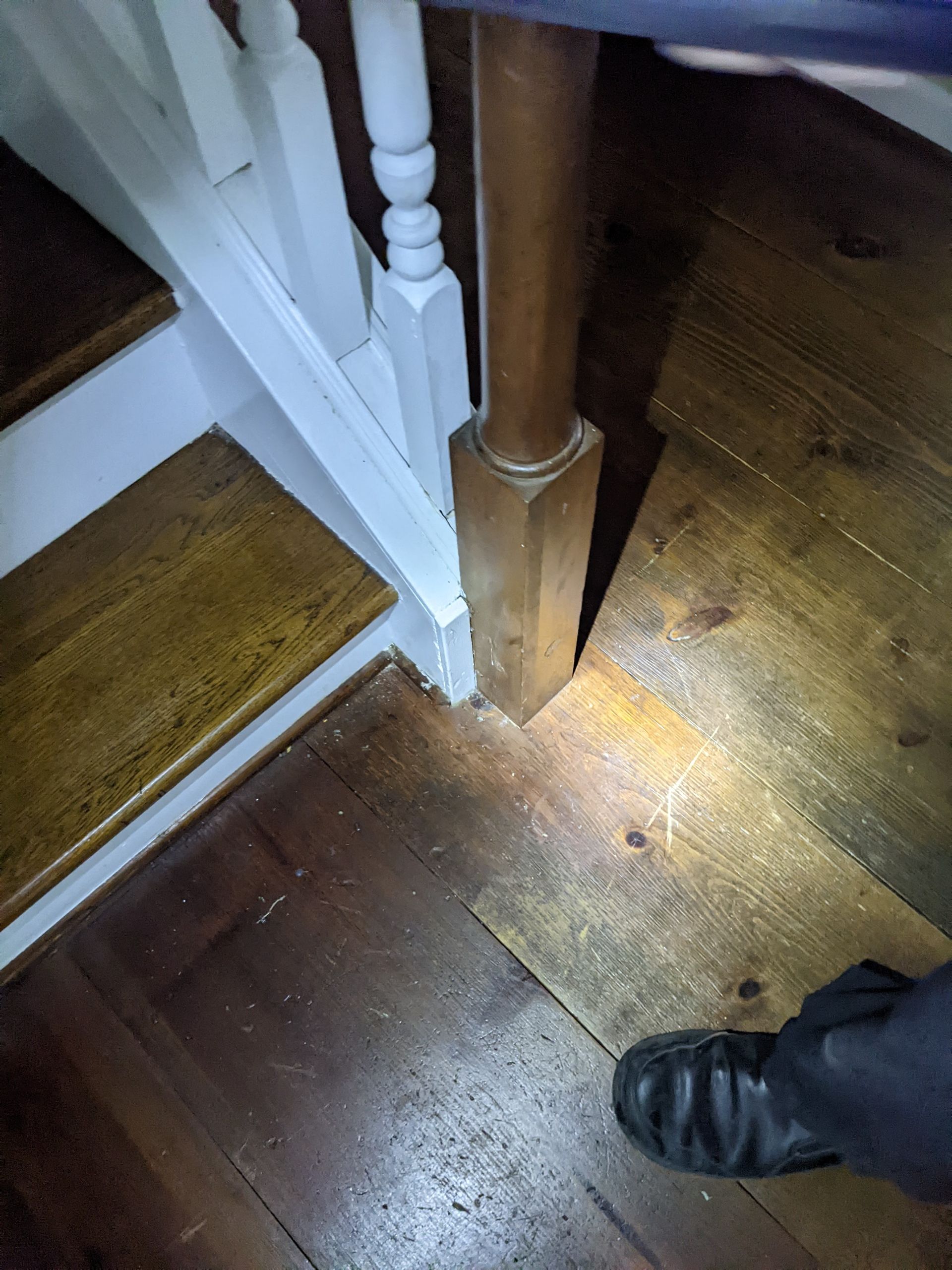 A person is standing under a staircase with a flashlight.