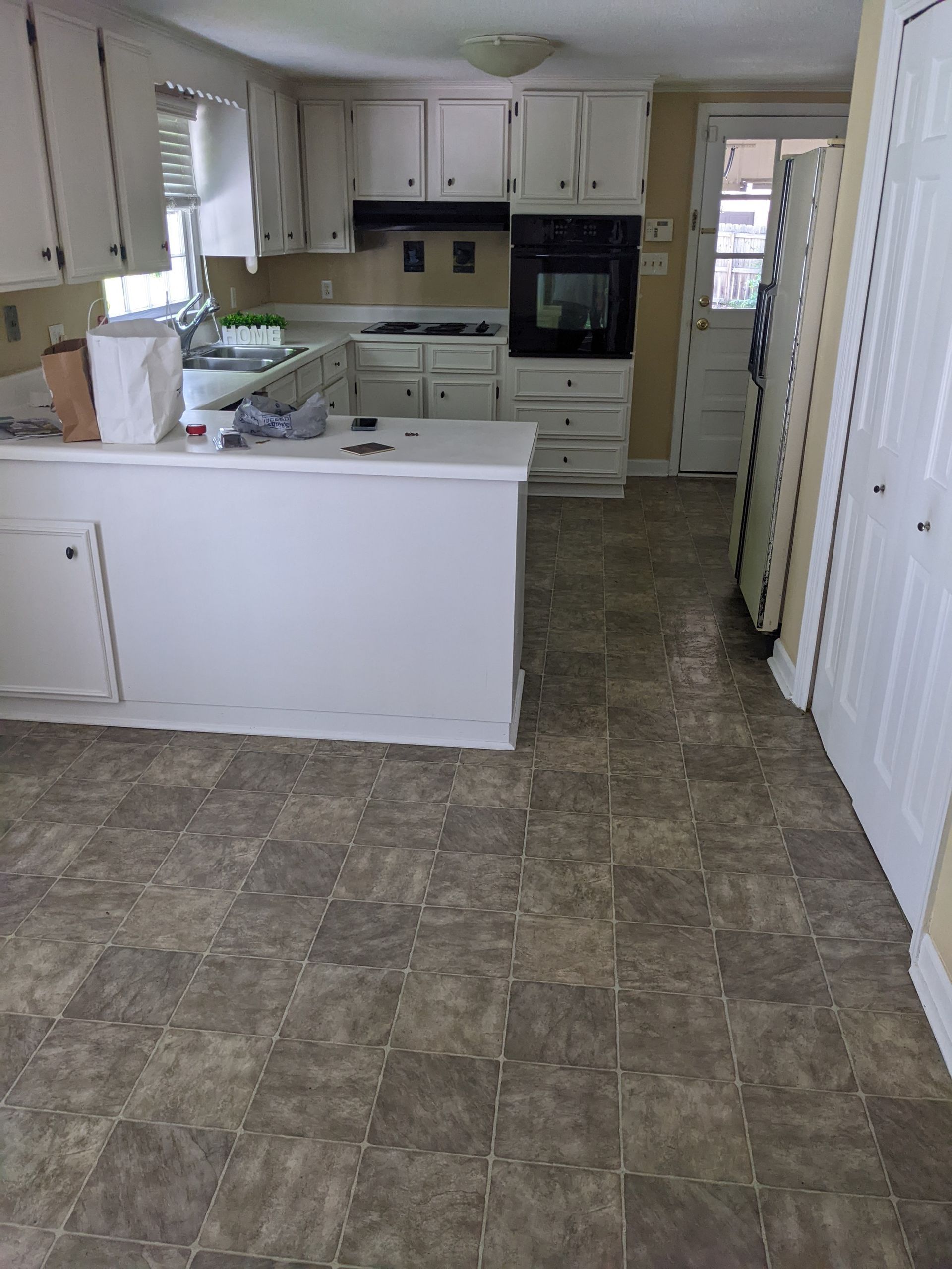 A kitchen with white cabinets and brown tile floors.