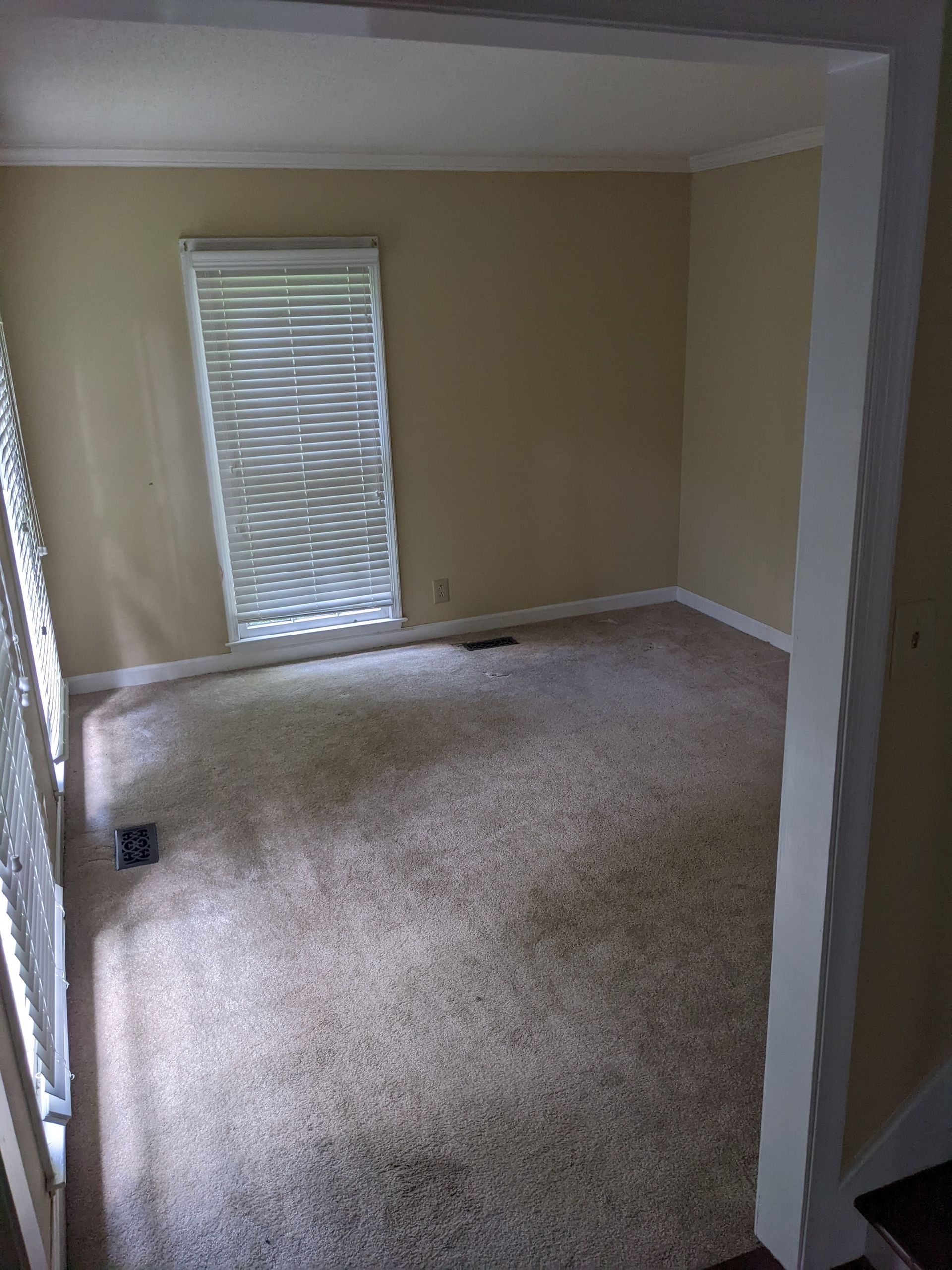 An empty living room with a carpeted floor and a window.