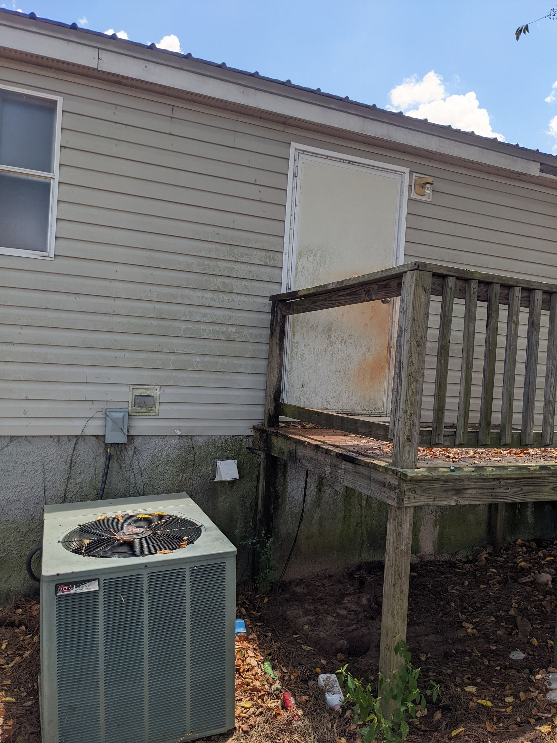 A mobile home with a deck and an air conditioner on the side of it.