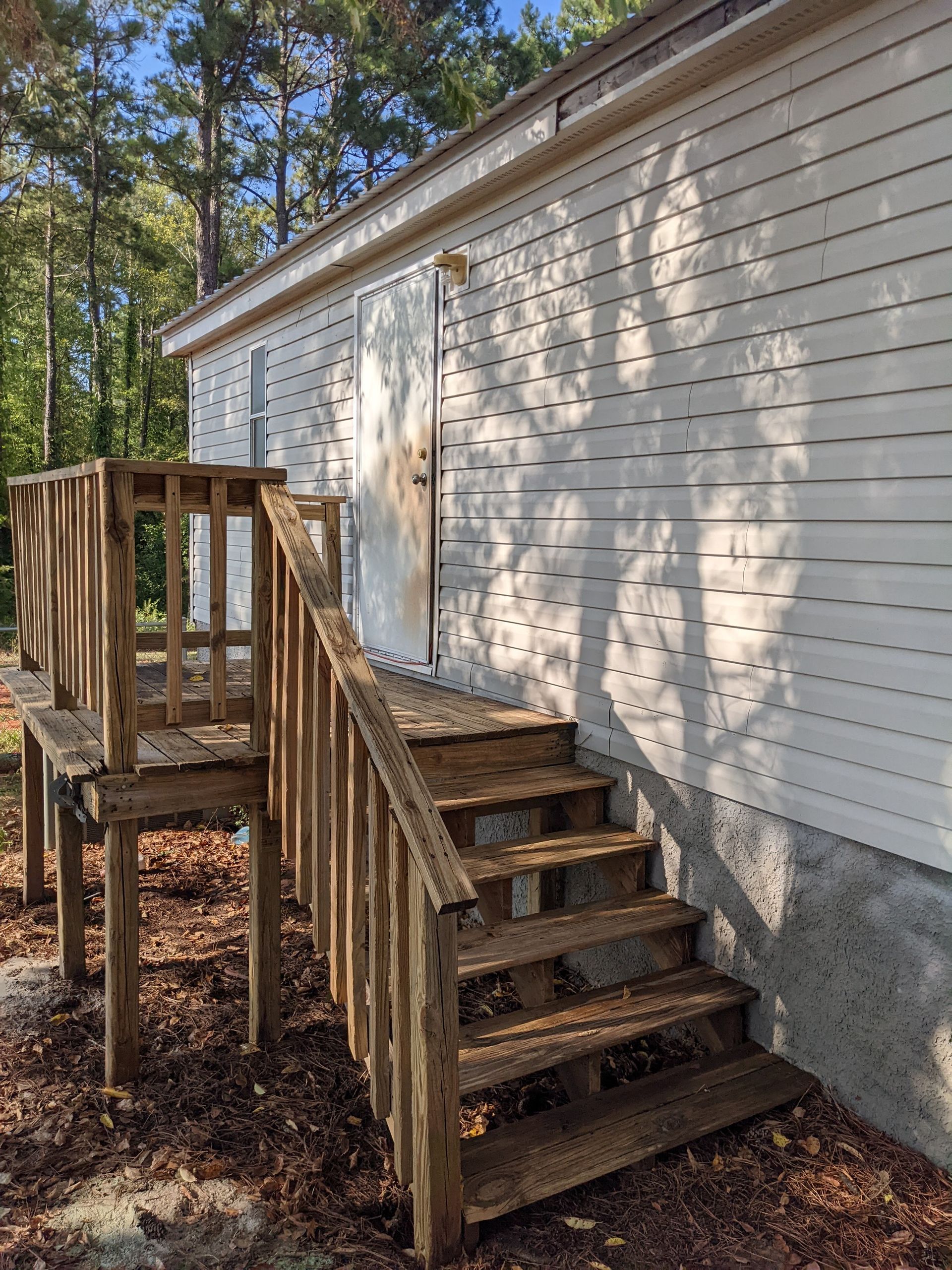A white mobile home with a wooden deck and stairs leading up to it.