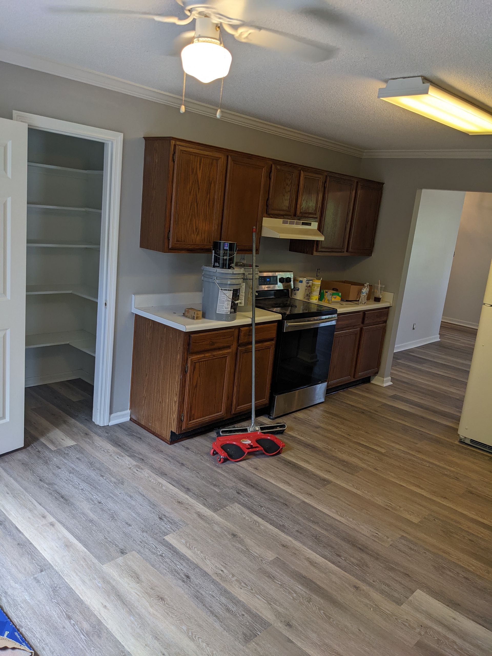 A kitchen with wooden cabinets , a stove , a refrigerator , and a ceiling fan.