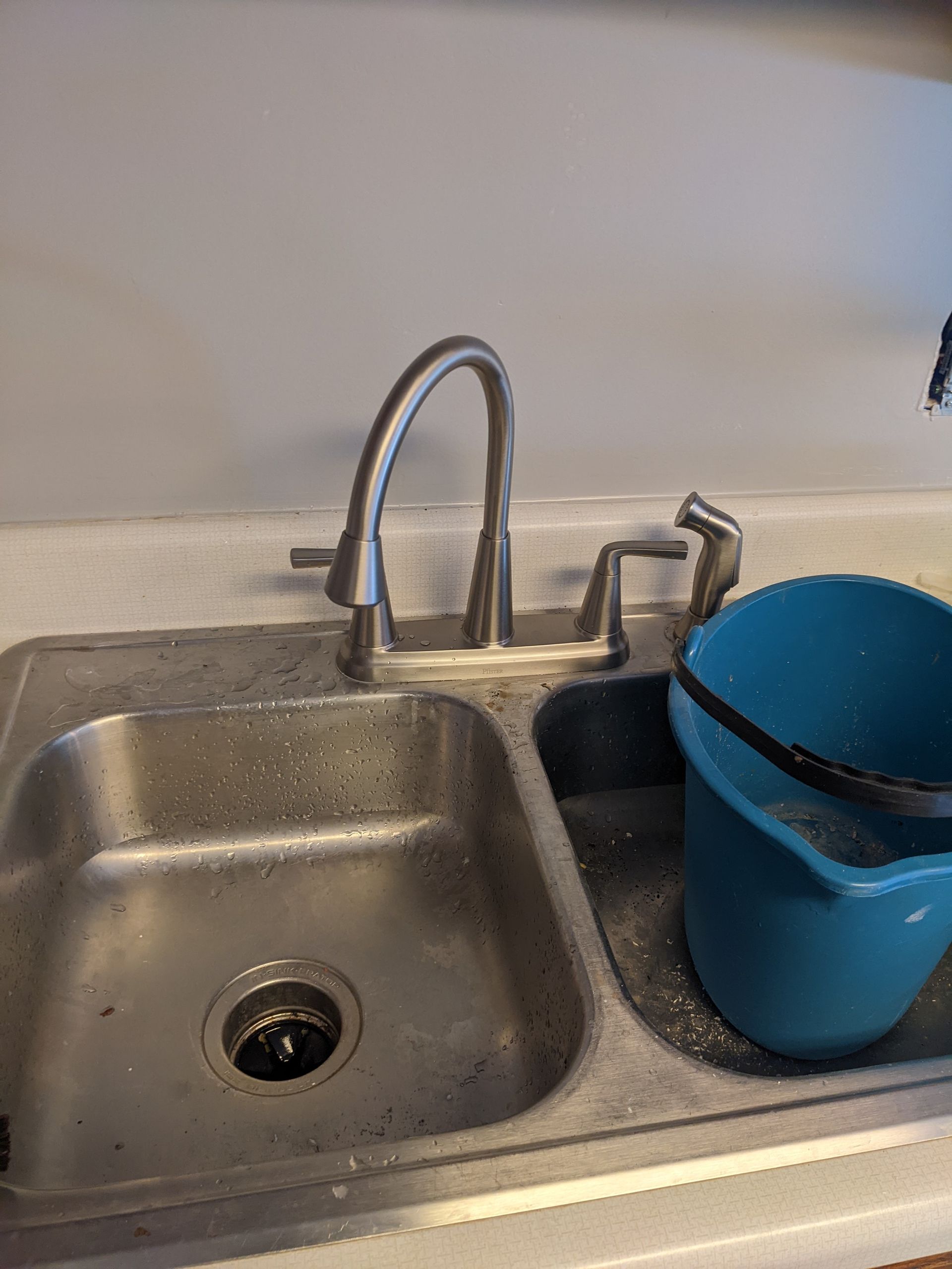 A stainless steel kitchen sink with a blue bucket underneath it.