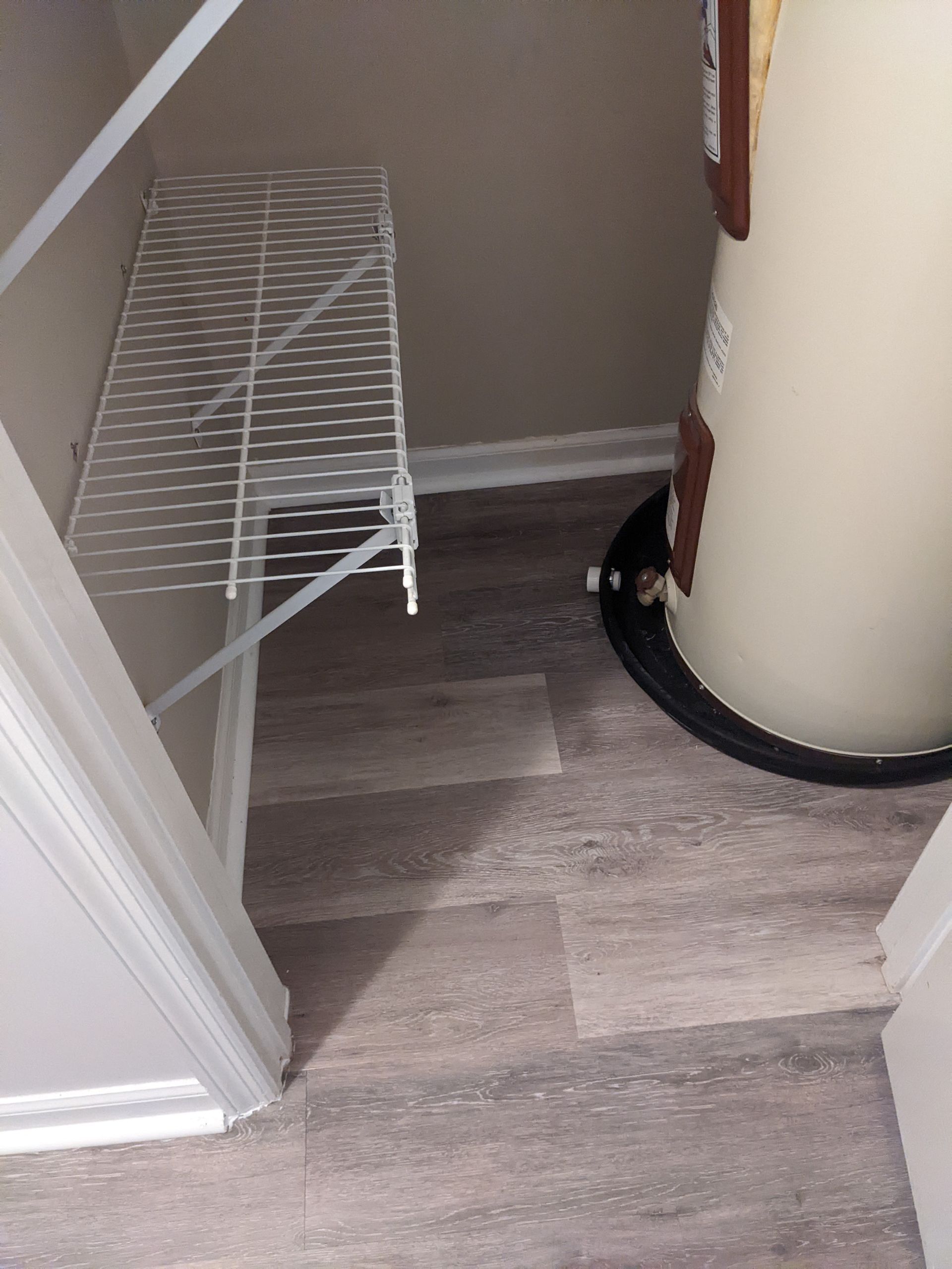 A water heater is sitting next to a shelf in a closet.