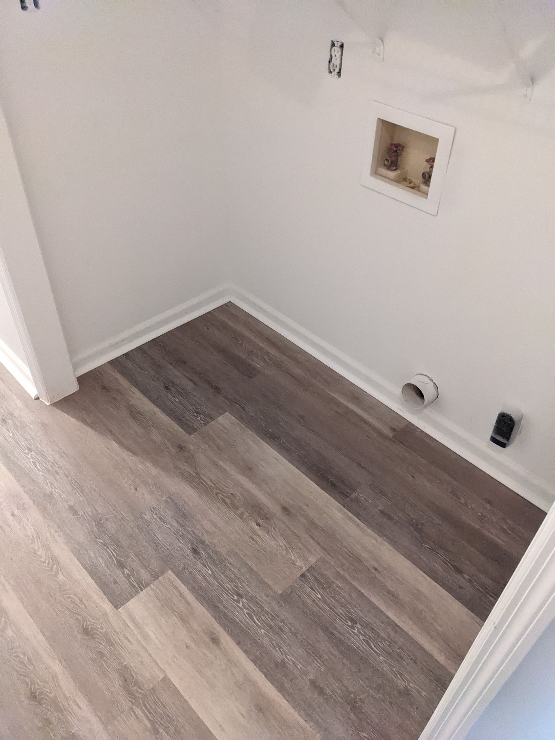A laundry room with hardwood floors and a white wall.