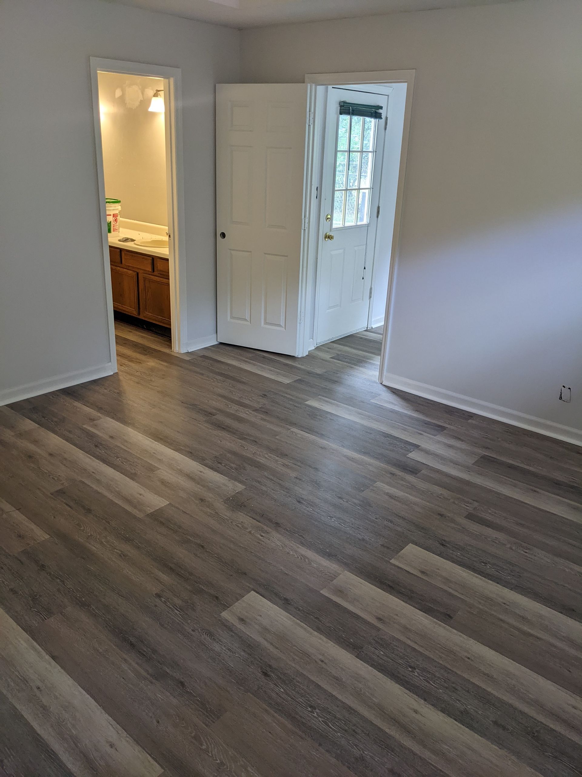A living room with hardwood floors and a bathroom in the background.