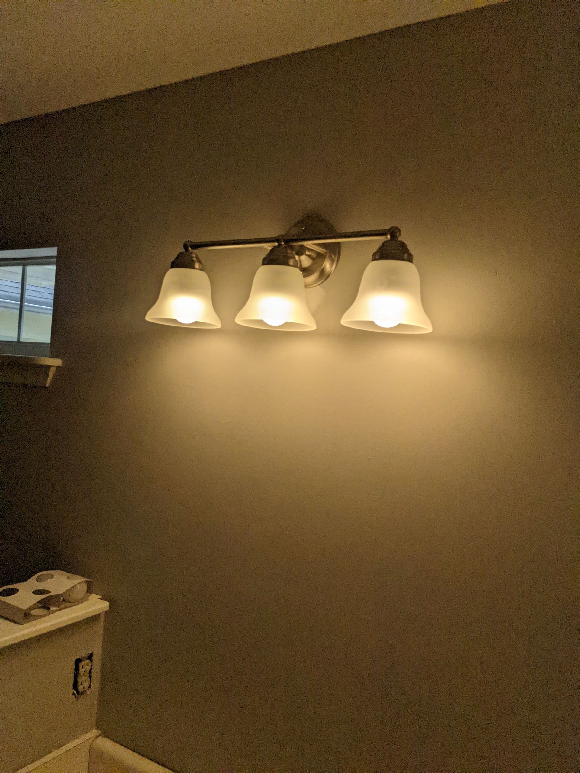 A bathroom vanity light is hanging on a wall next to a toilet.