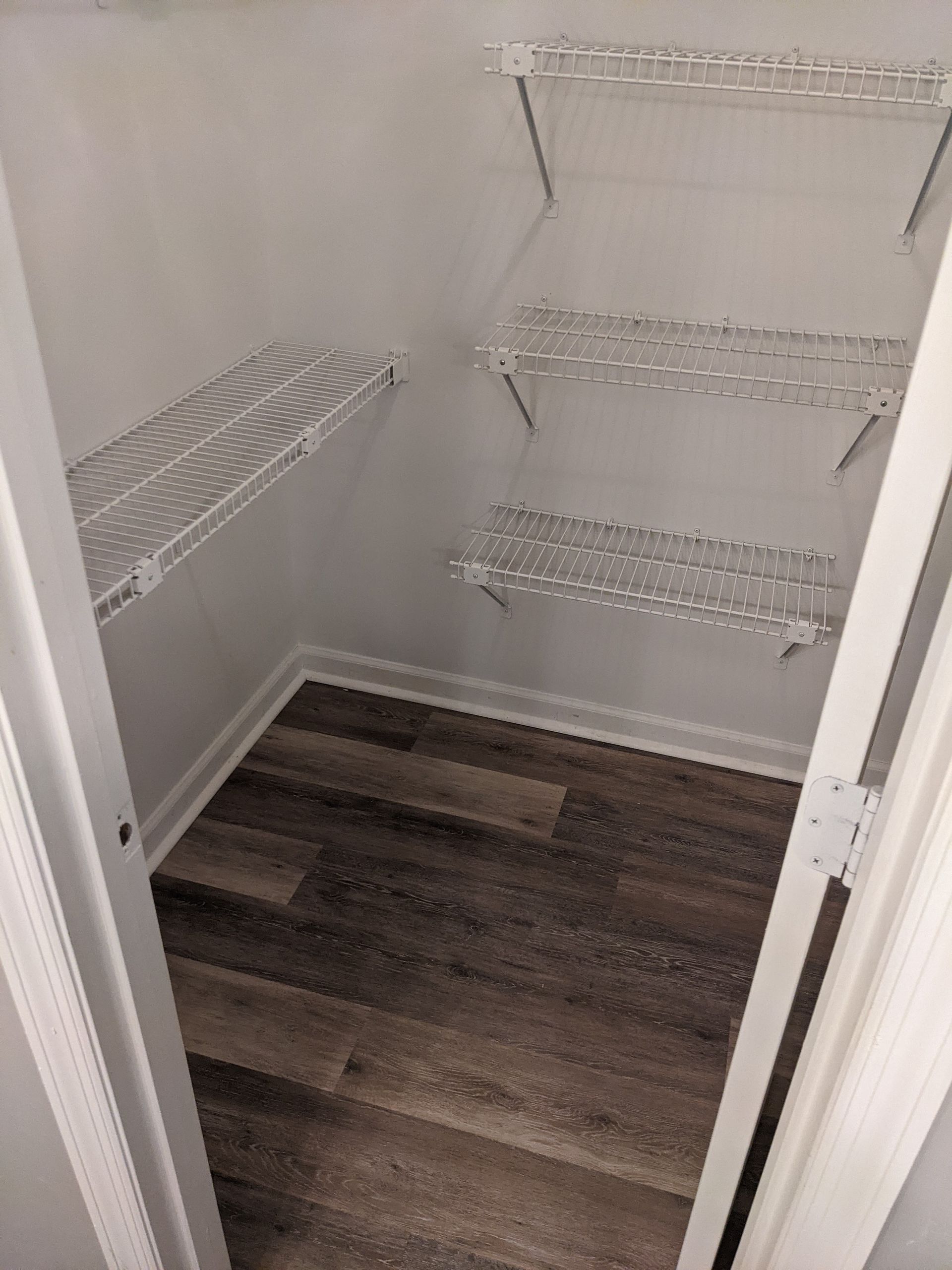 A walk in closet with wooden floors and white shelves.