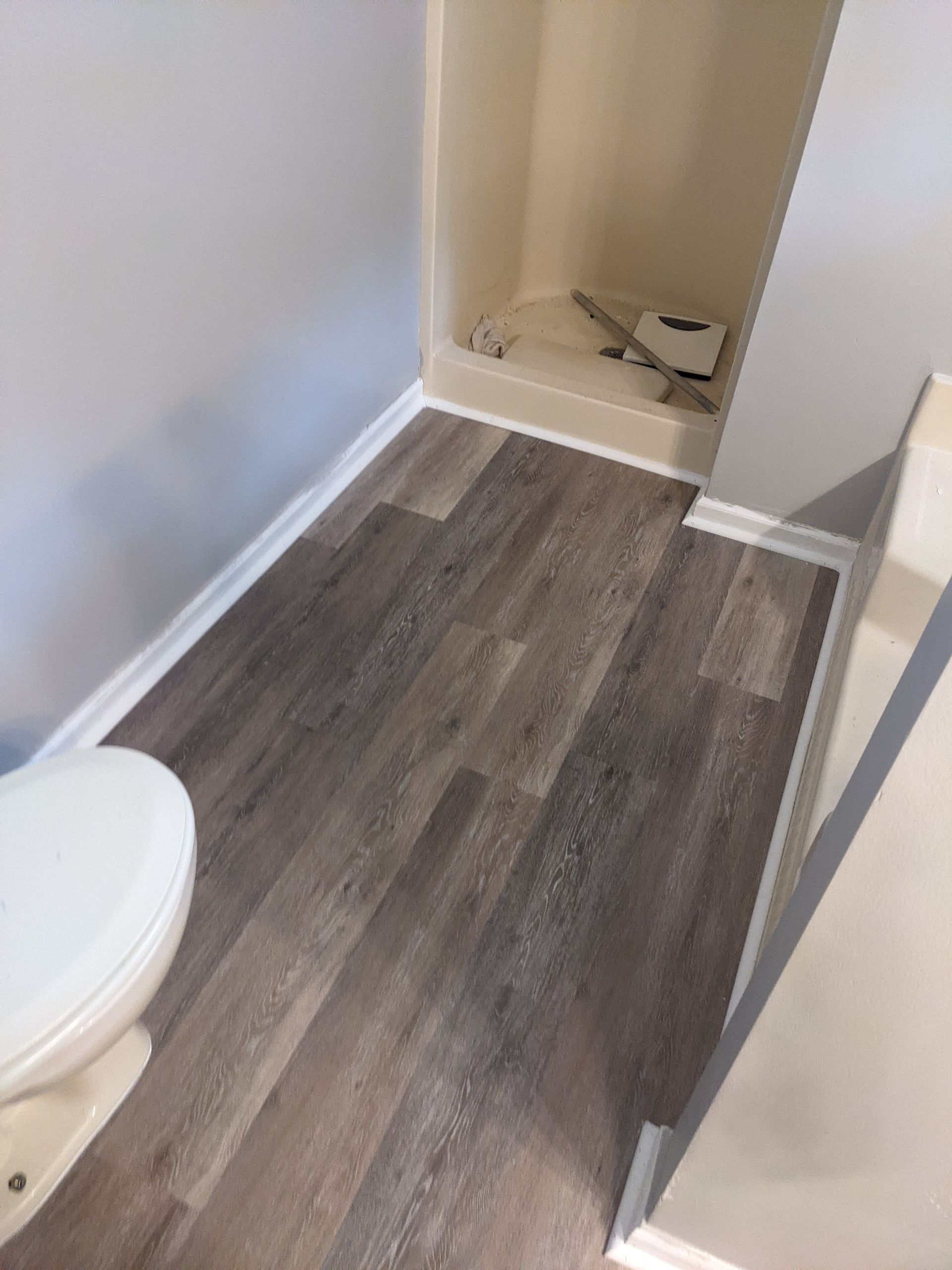 A bathroom with a toilet , shower and wooden floor.