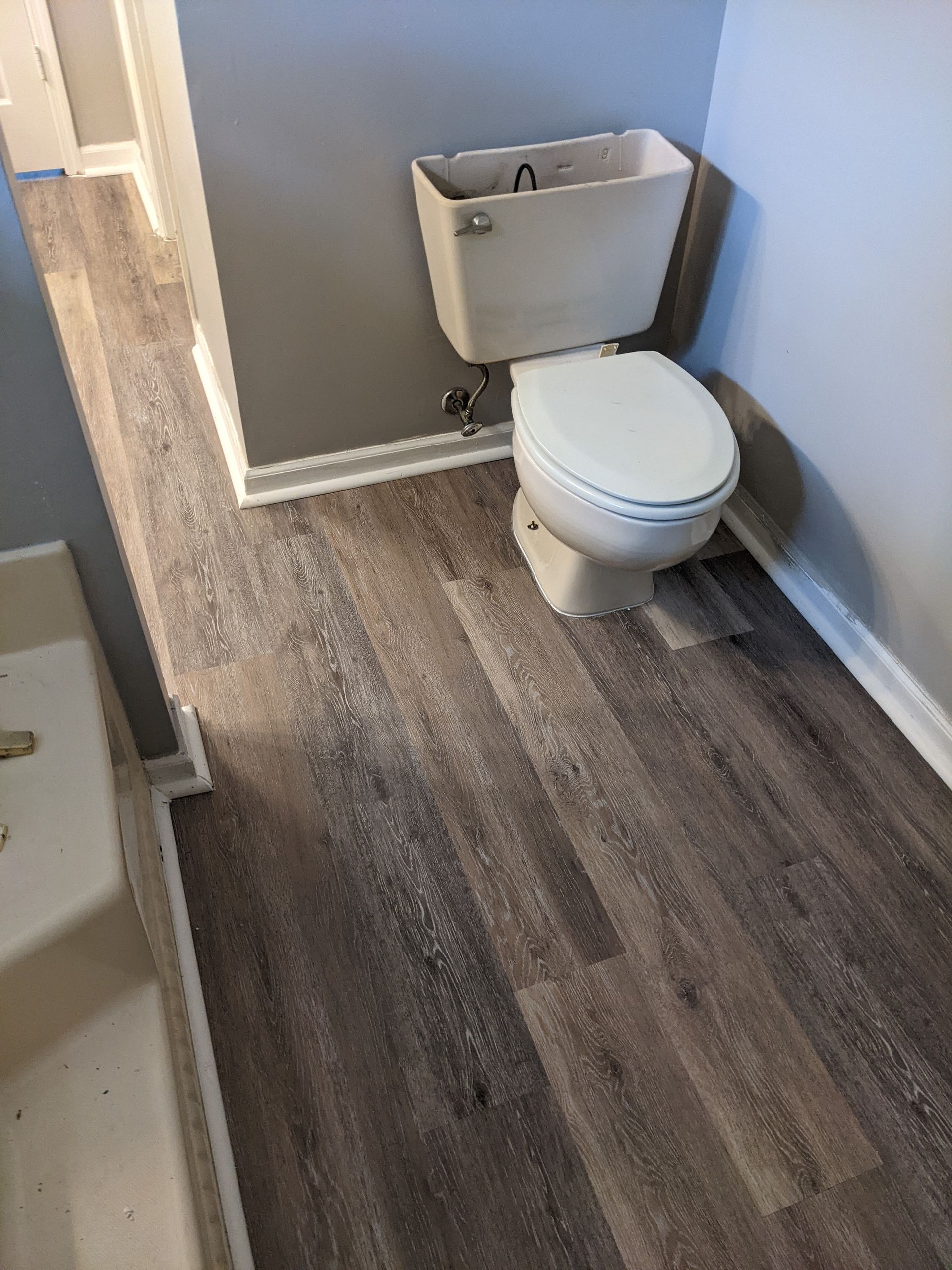 A toilet is sitting on a wooden floor in a bathroom.