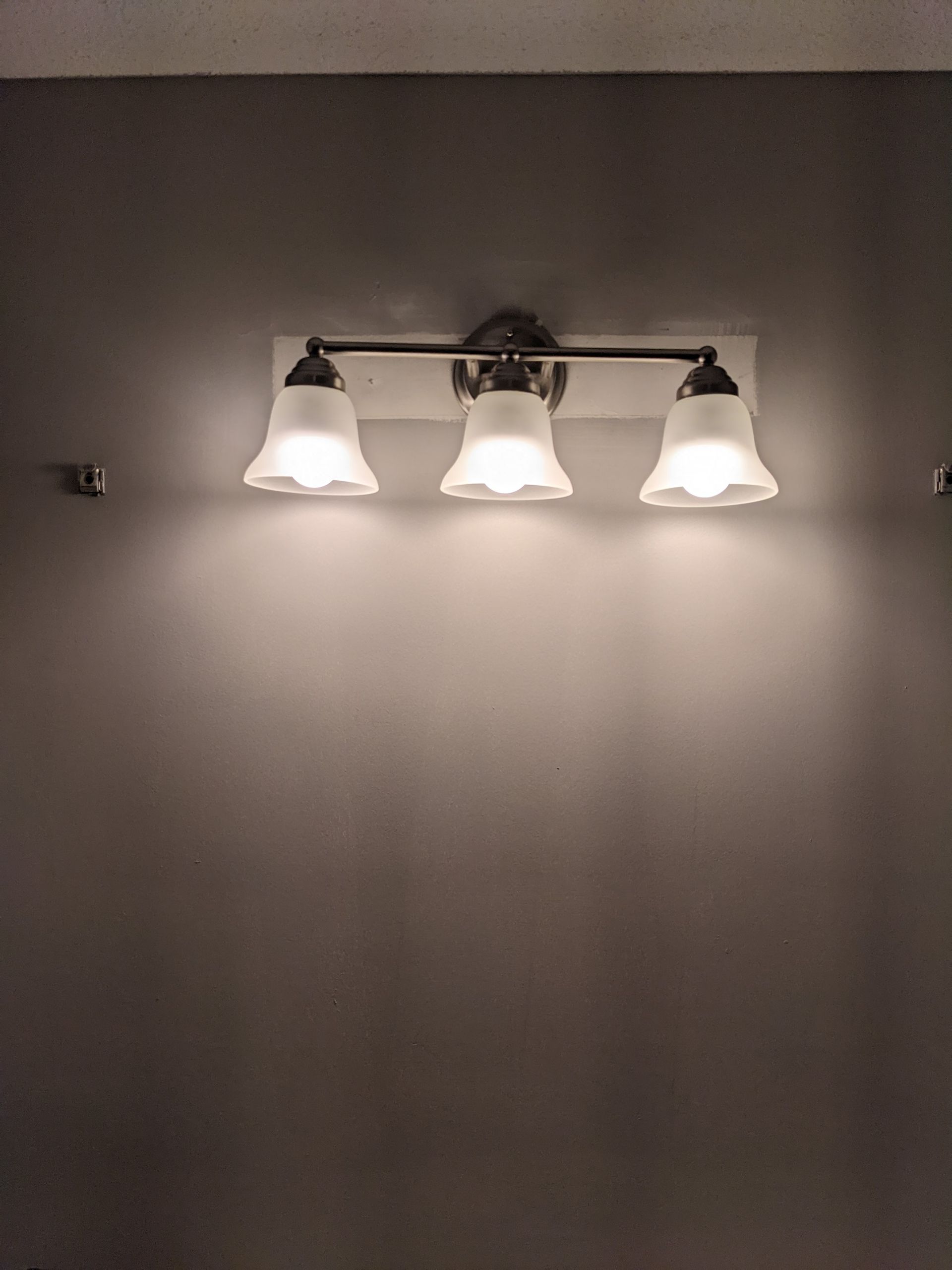 A bathroom vanity light is hanging on a gray wall.