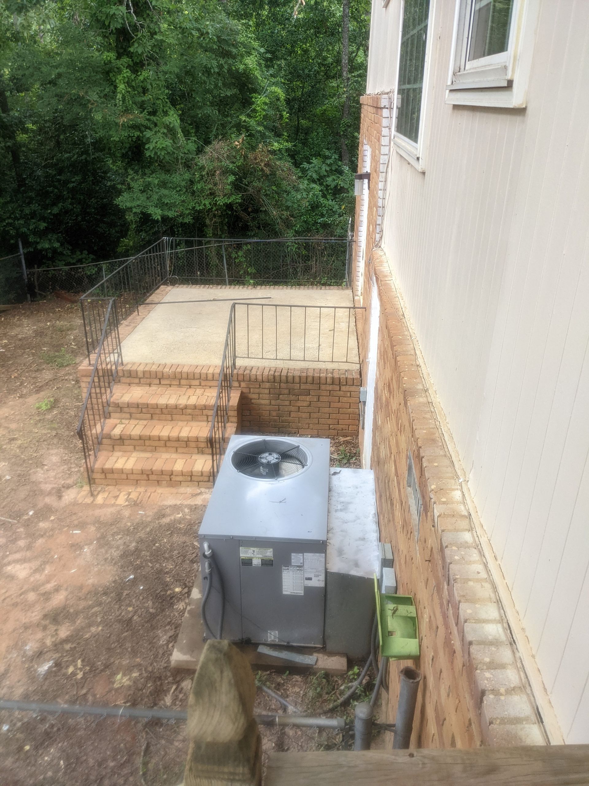 An air conditioner is sitting on the side of a house next to stairs.