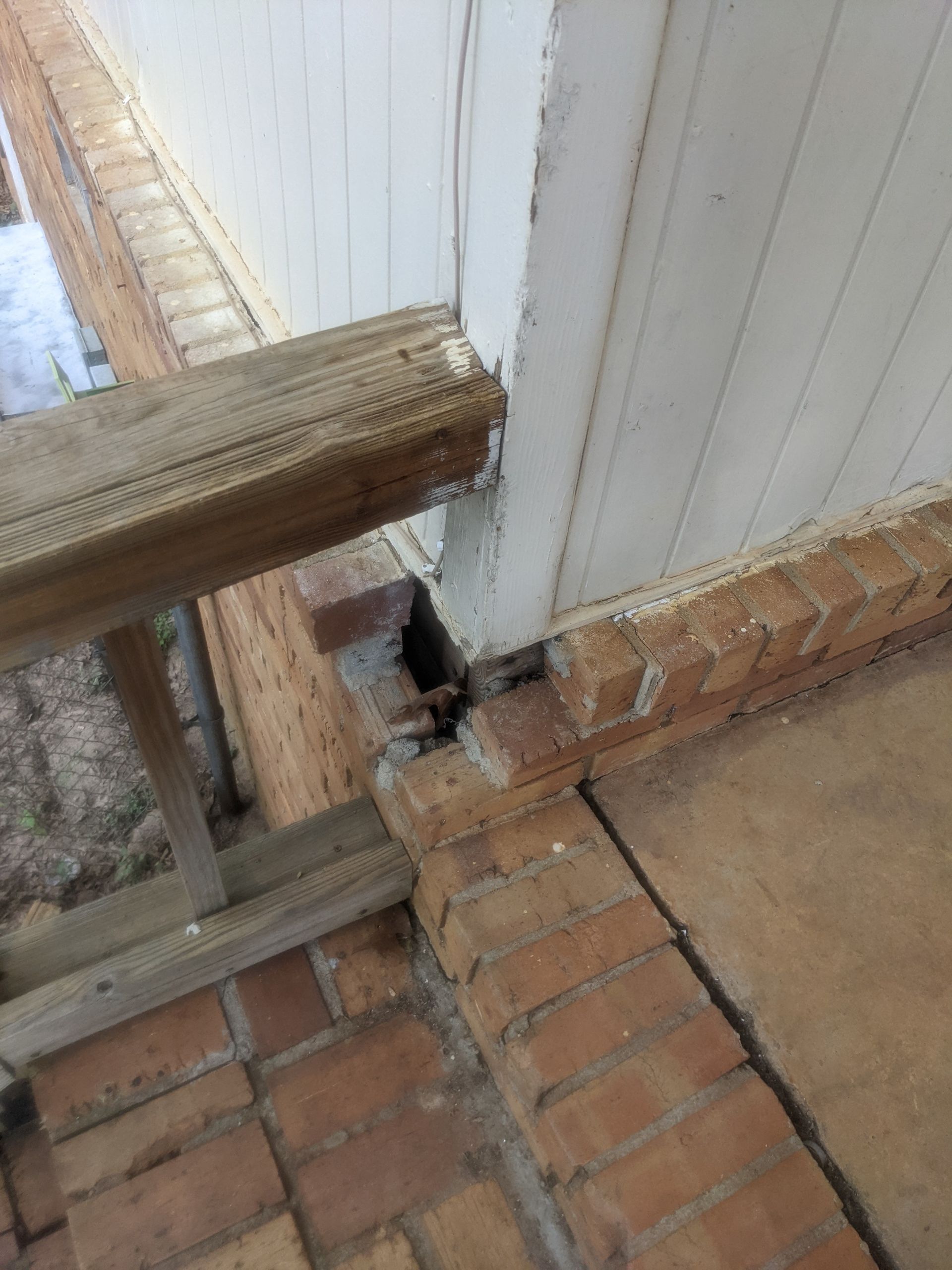 A wooden railing is sitting next to a brick wall.