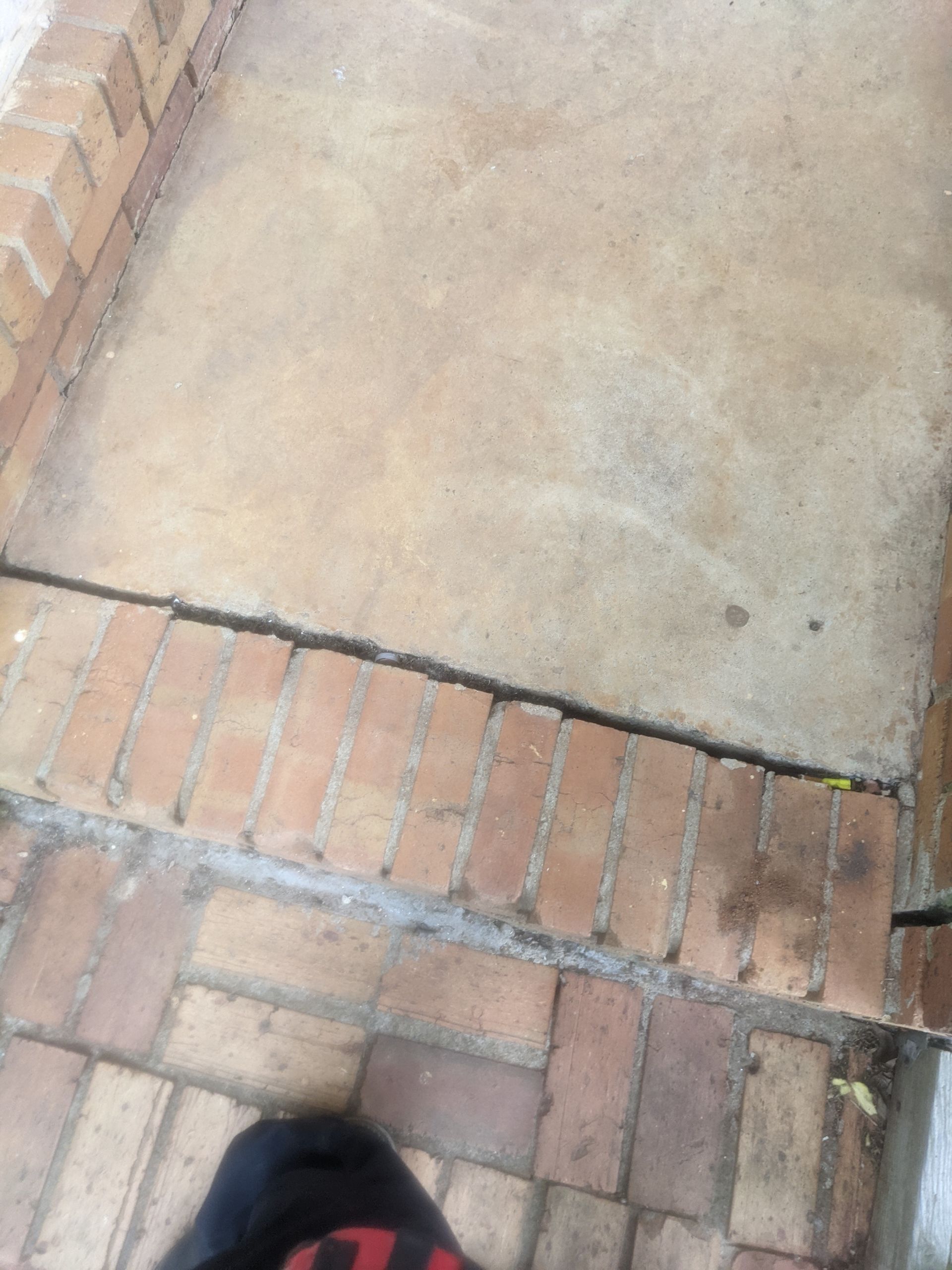 A person standing on a sidewalk with bricks and concrete