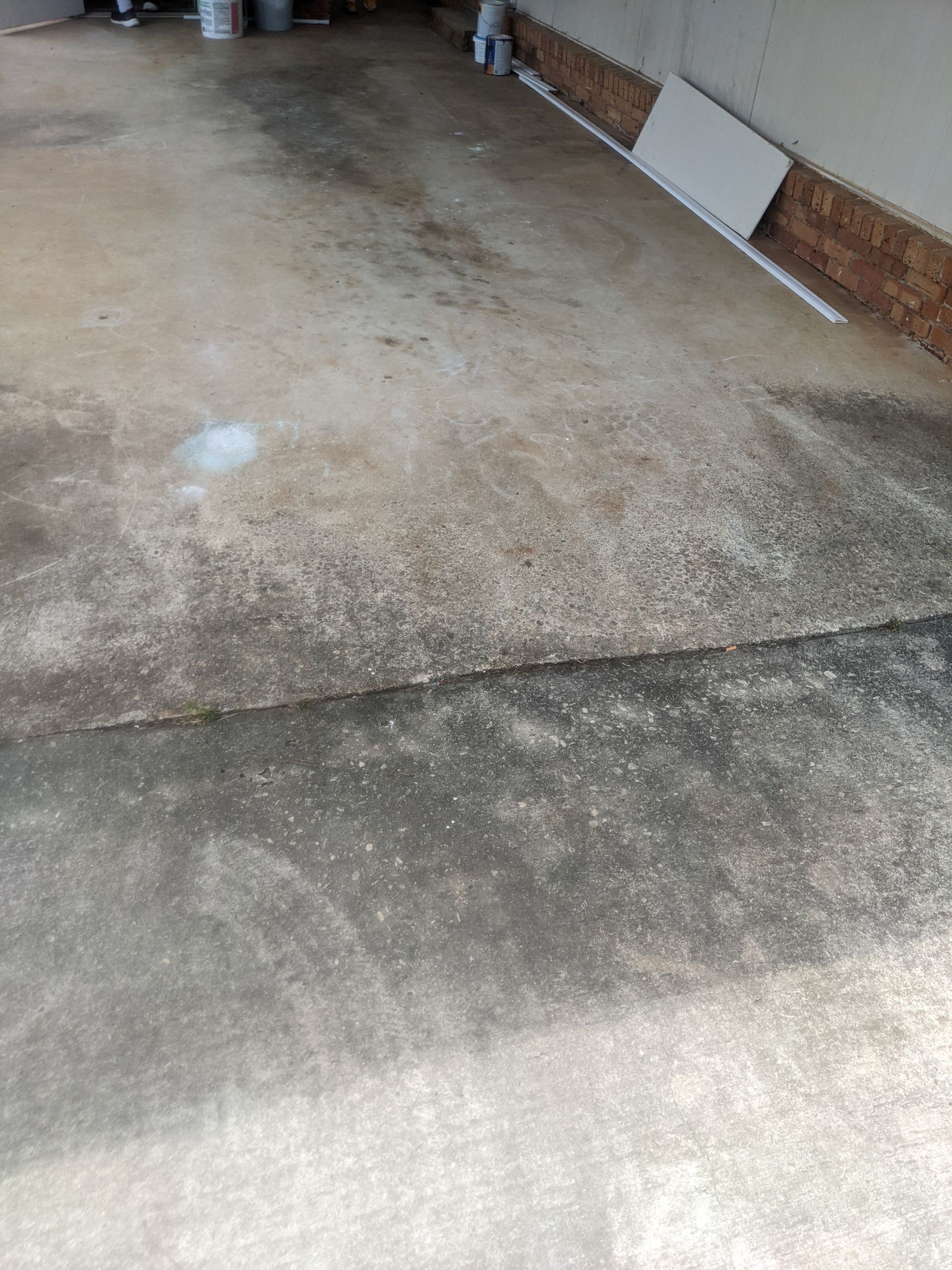 A dirty concrete floor in a driveway next to a brick wall.