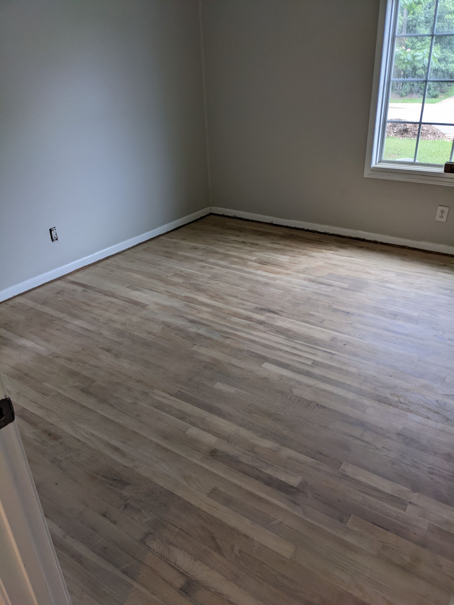 A bedroom with hardwood floors and a window.