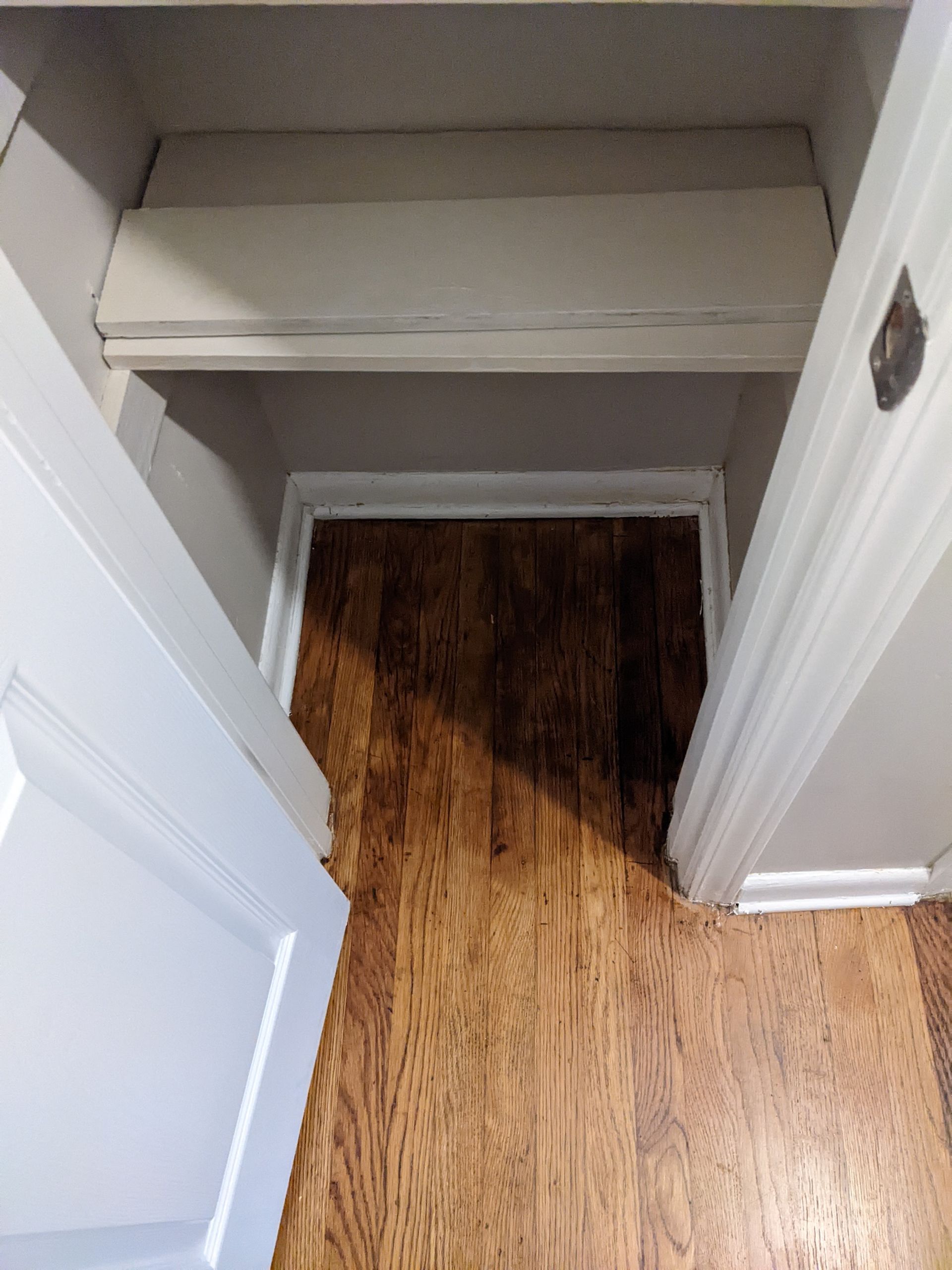 A closet with hardwood floors and a shelf in it.