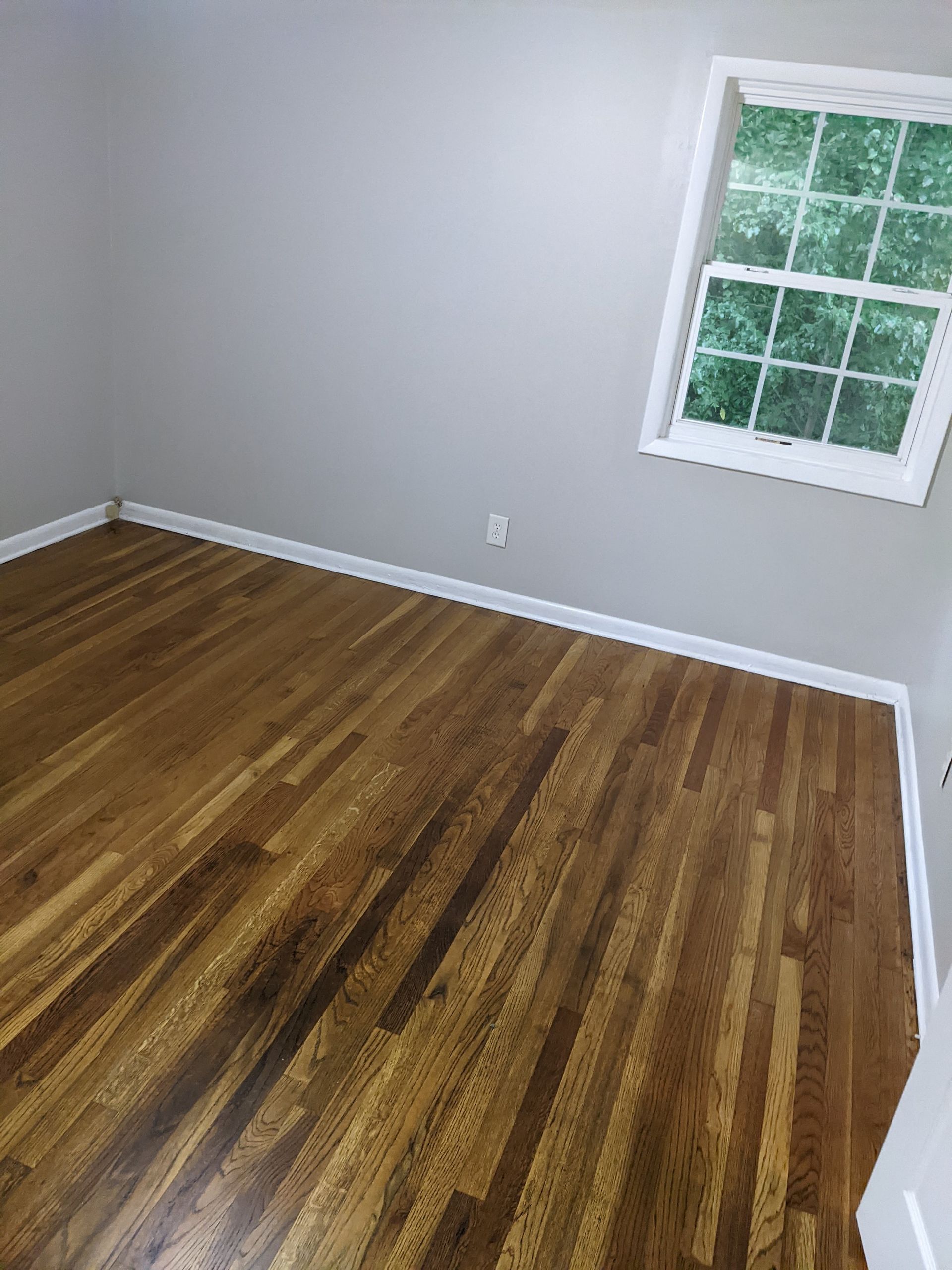 A bedroom with hardwood floors and a window.