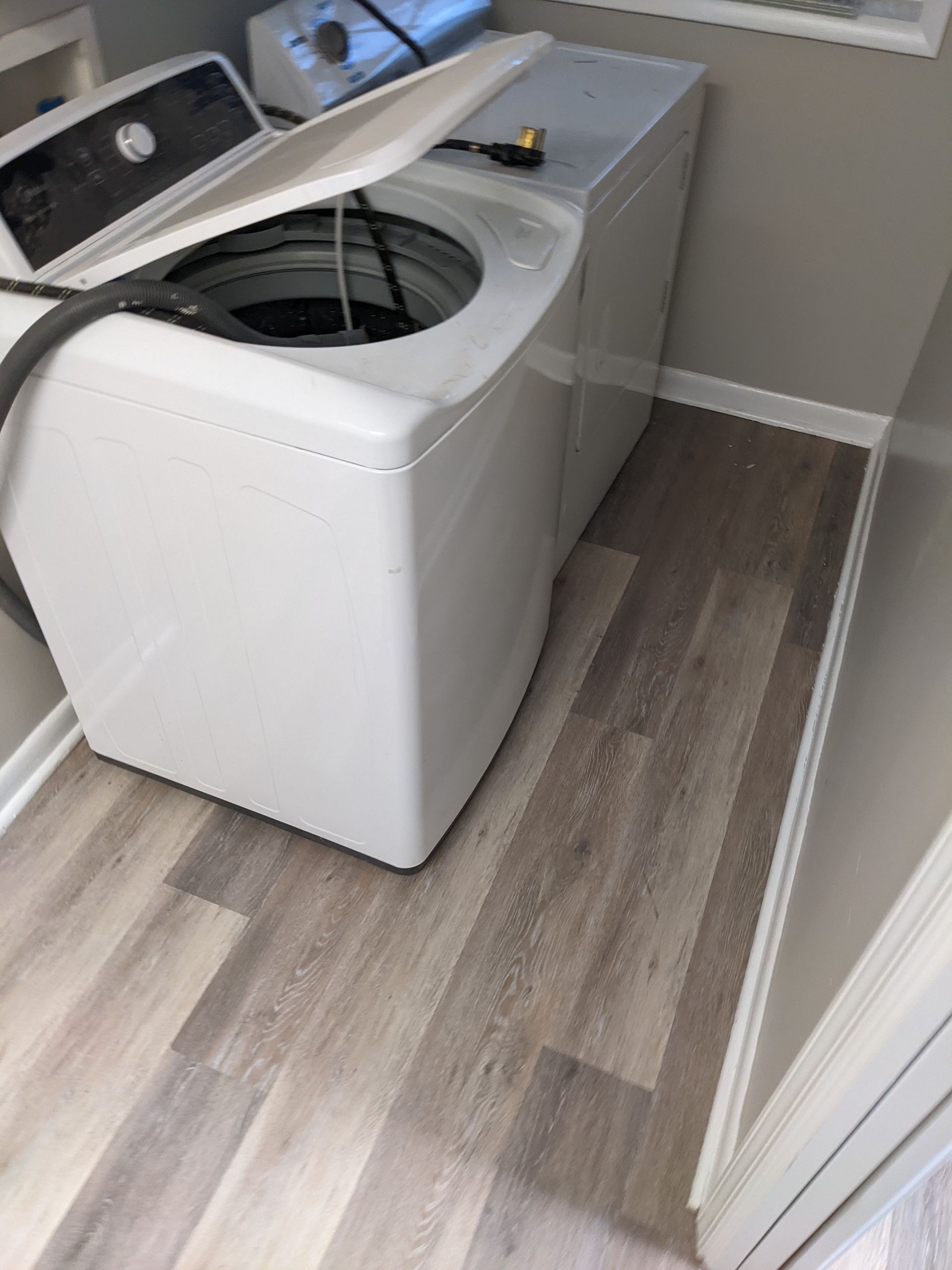 A washer and dryer are sitting on a wooden floor in a laundry room.