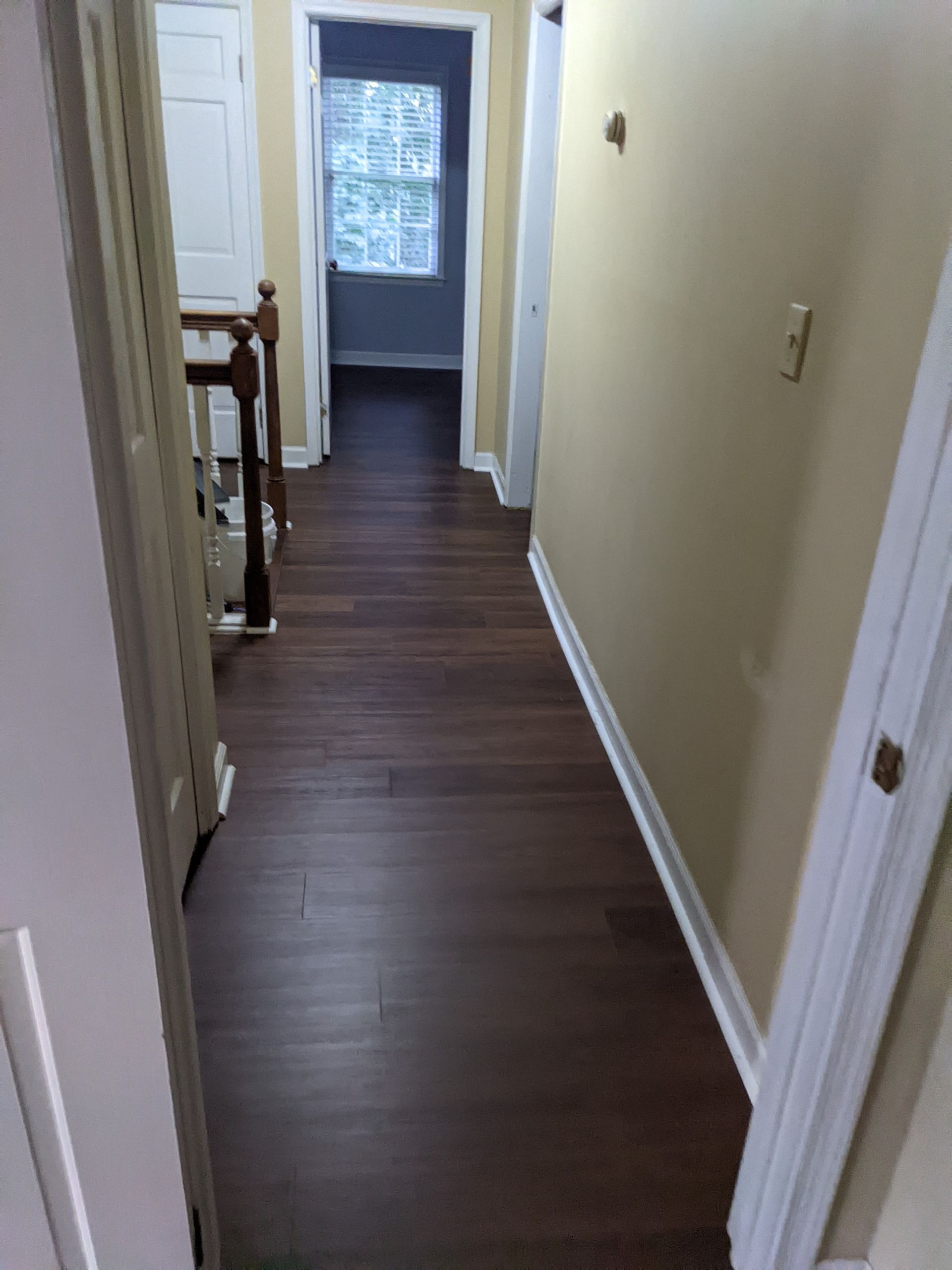 A hallway with hardwood floors and a staircase in a house.