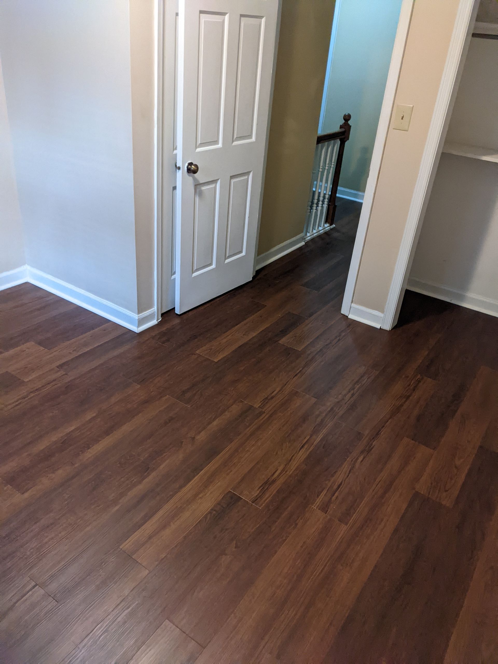 A hallway with a wooden floor and a door leading to a staircase.