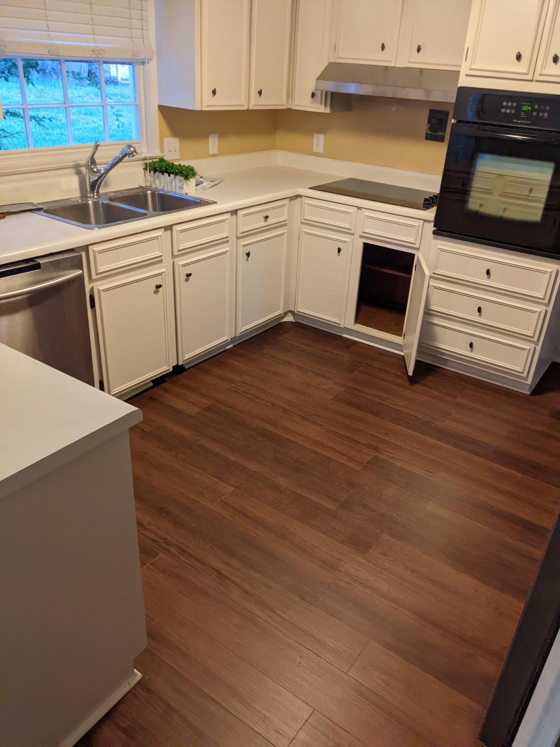 A kitchen with white cabinets , stainless steel appliances , hardwood floors and a sink.