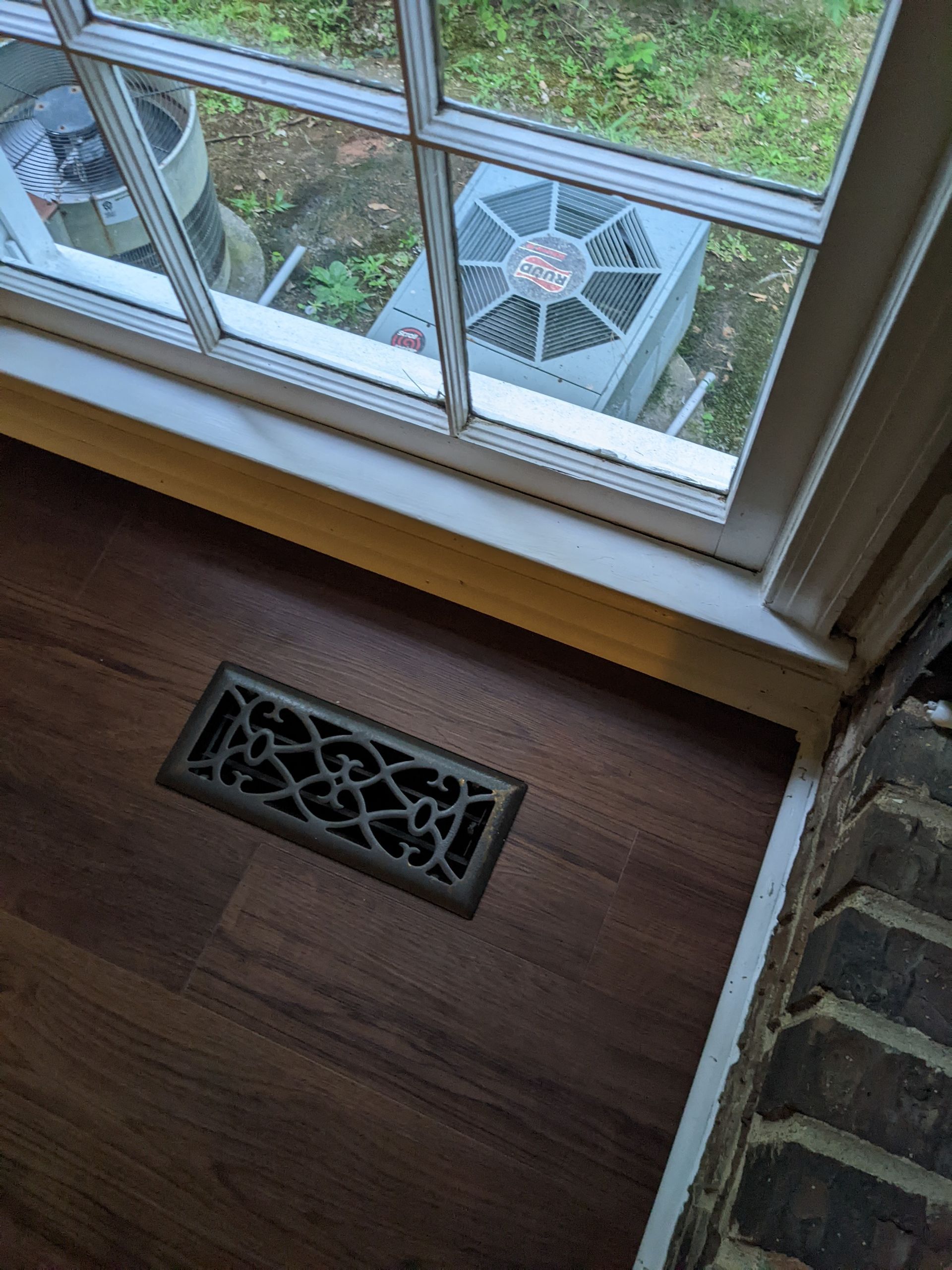 A fan is sitting under a window next to a wooden floor.