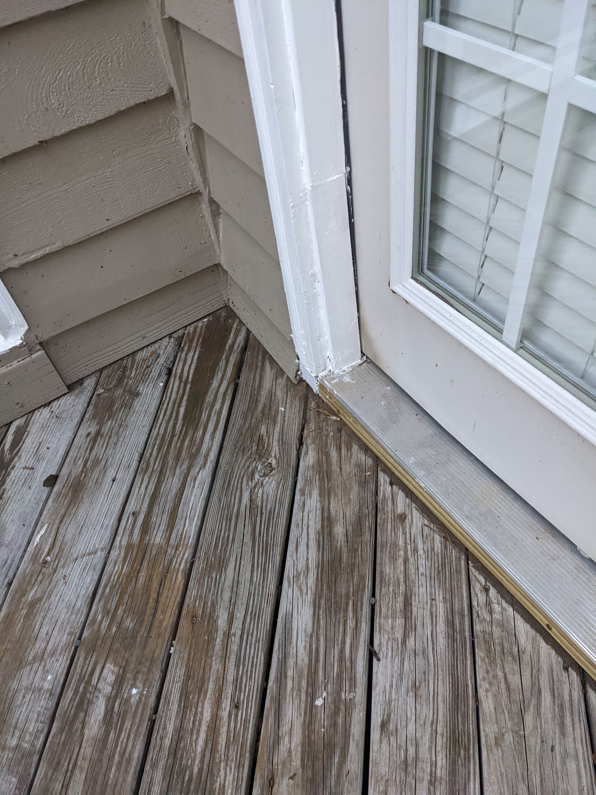 A wooden deck with a sliding glass door next to a house.