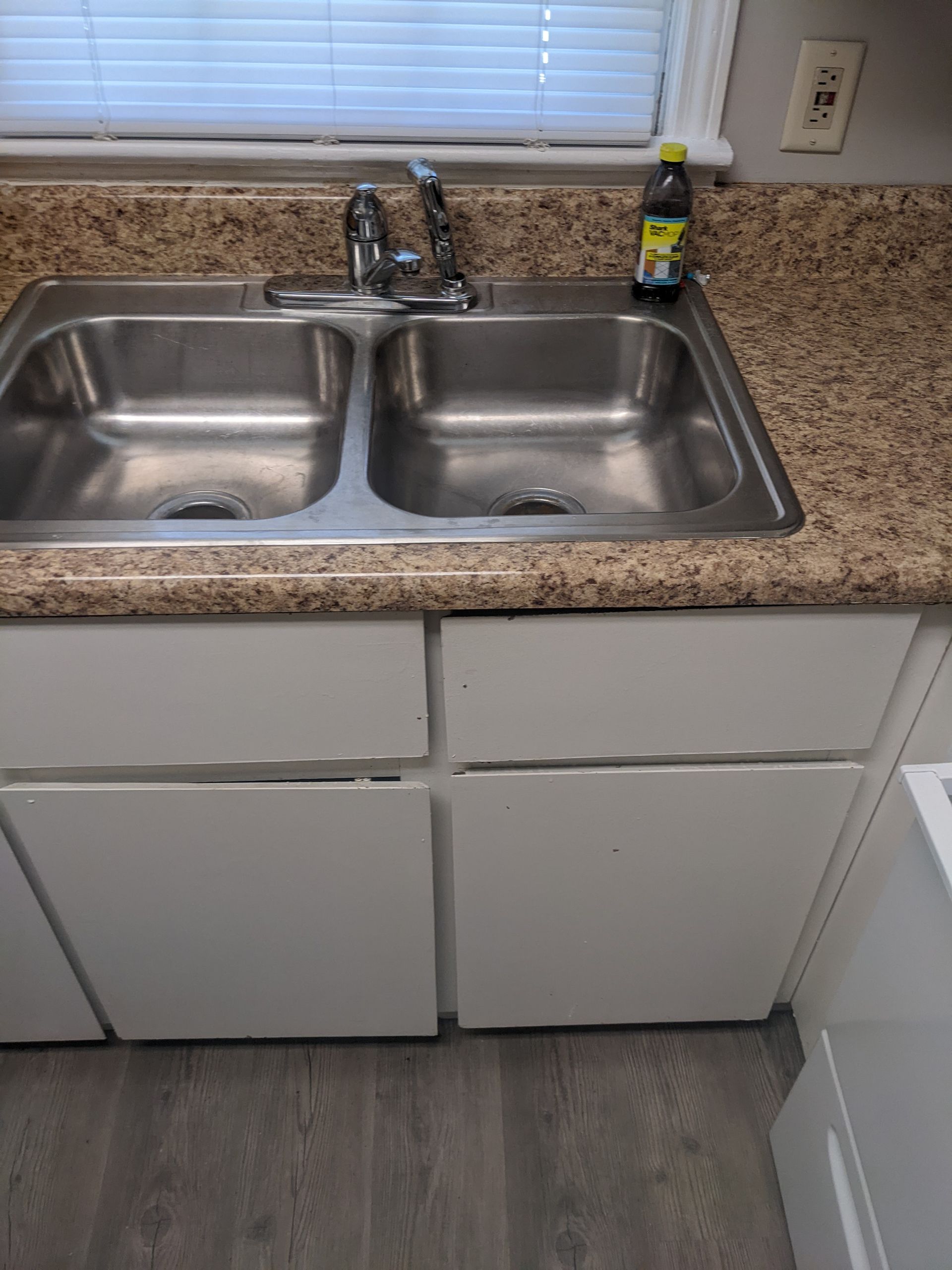 A kitchen sink with a bottle of cleaner on the counter.