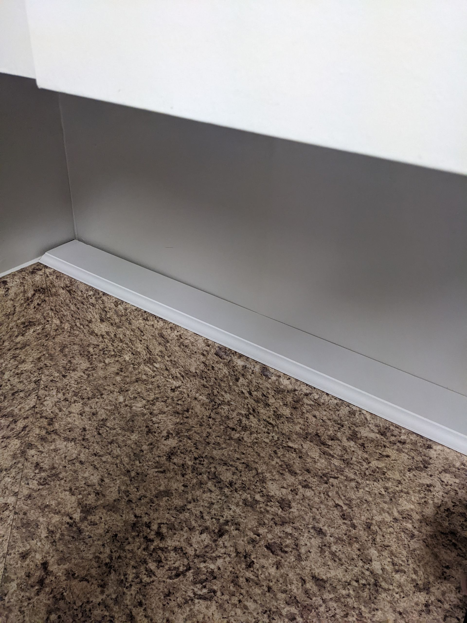 A corner of a room with a brown carpet and a white wall.