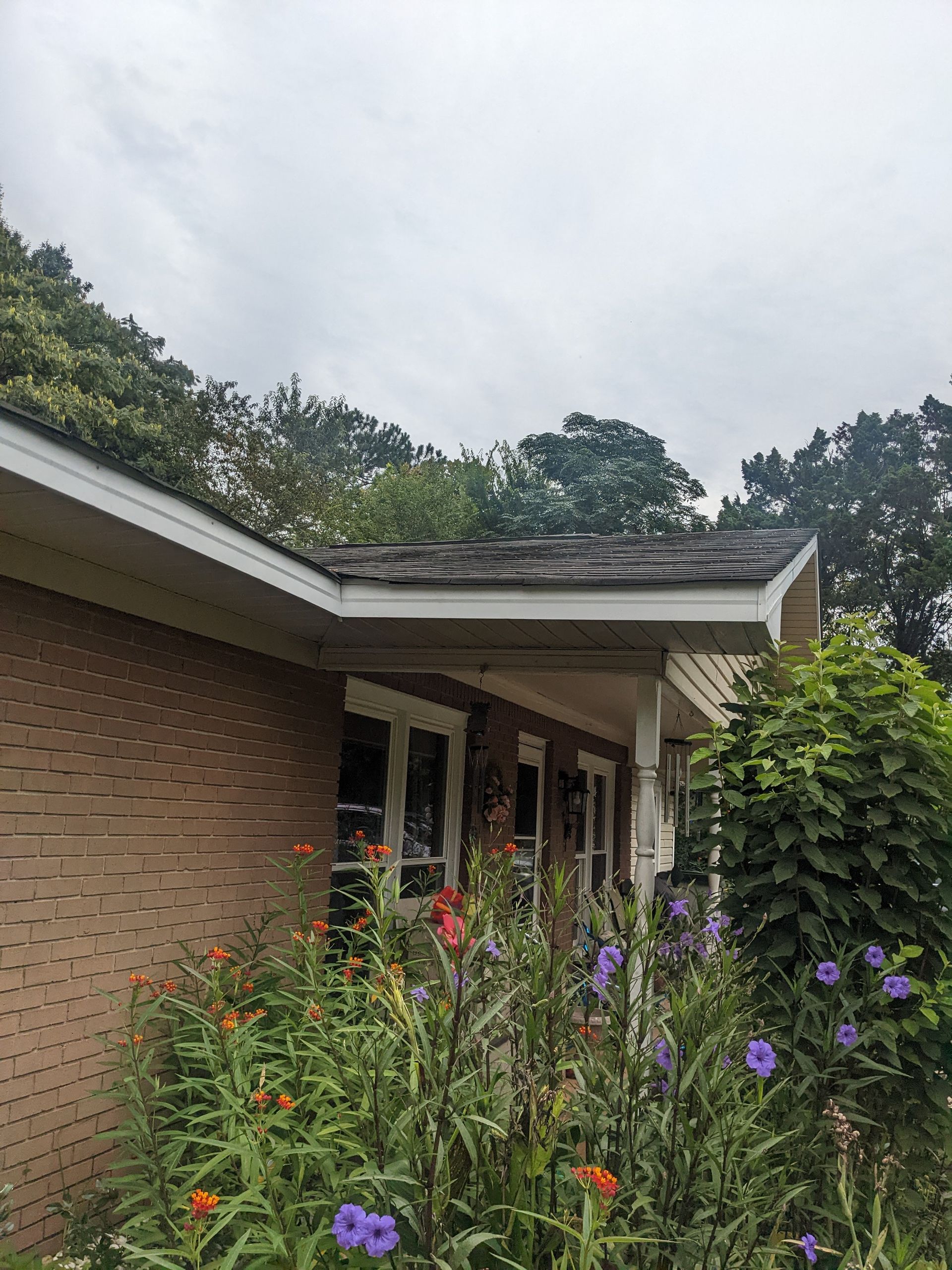A brick house with a porch and flowers in front of it.