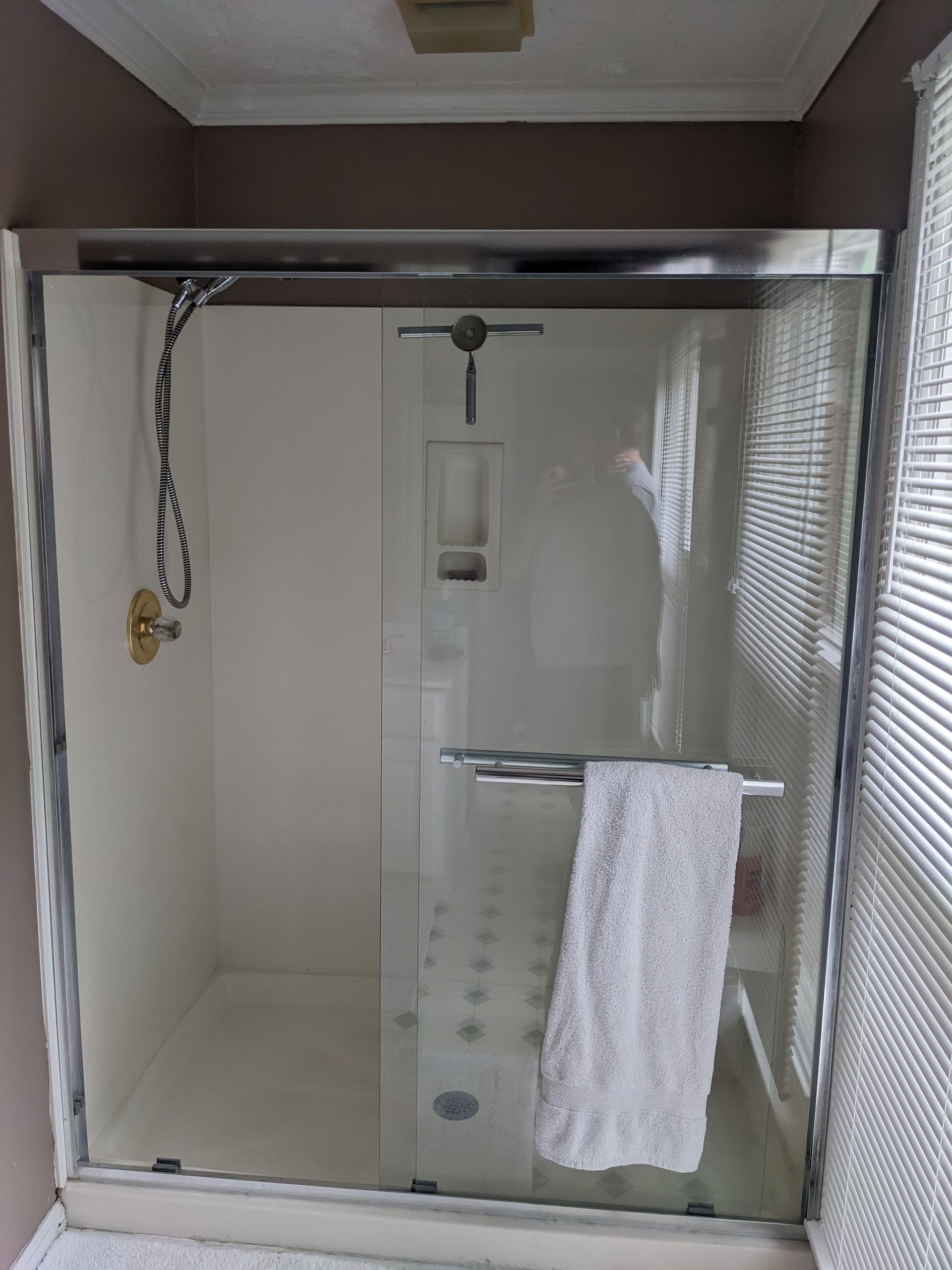 A bathroom with a sliding glass shower door and a towel on the railing.