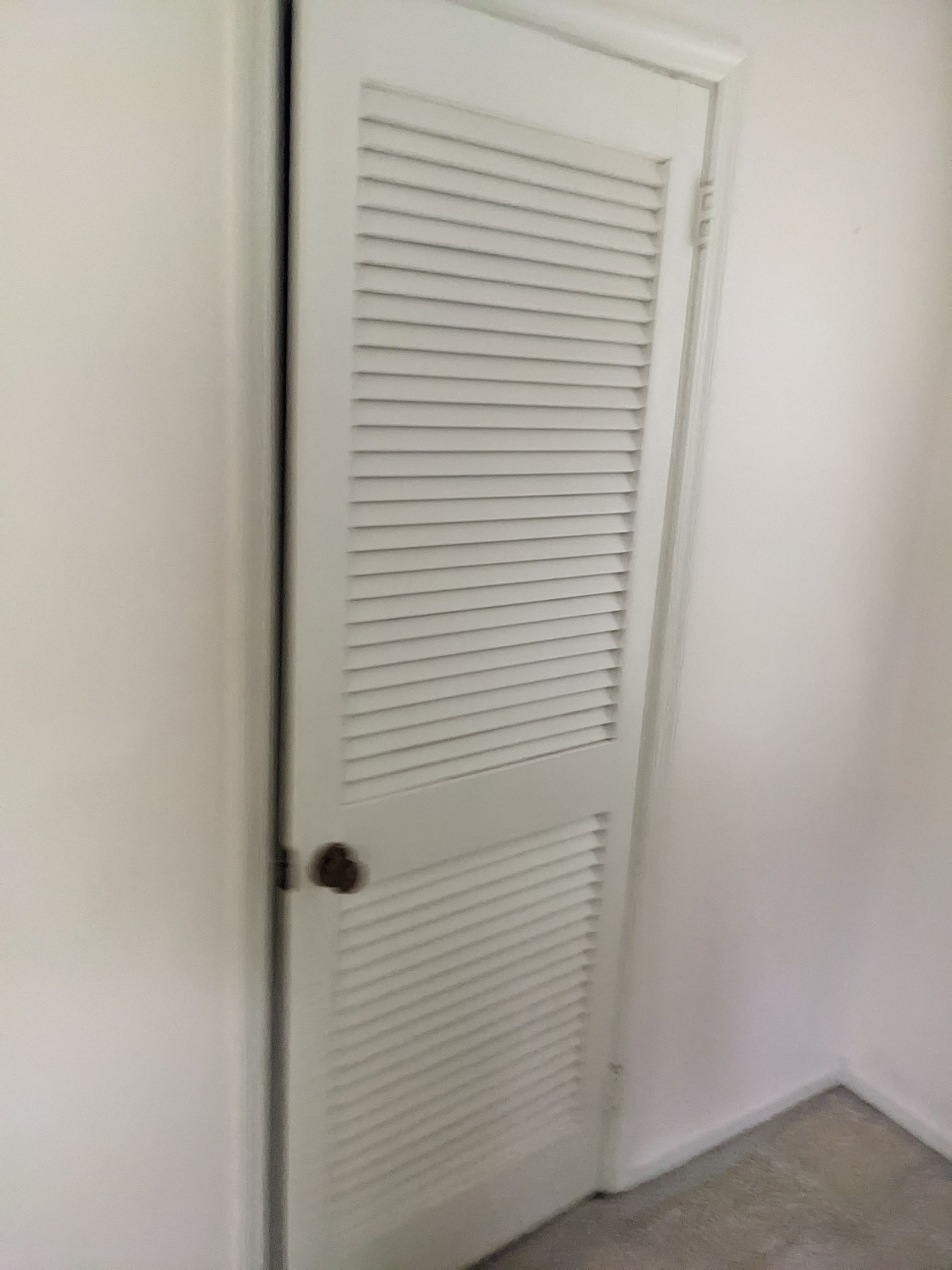 A white closet door with shutters in a room.