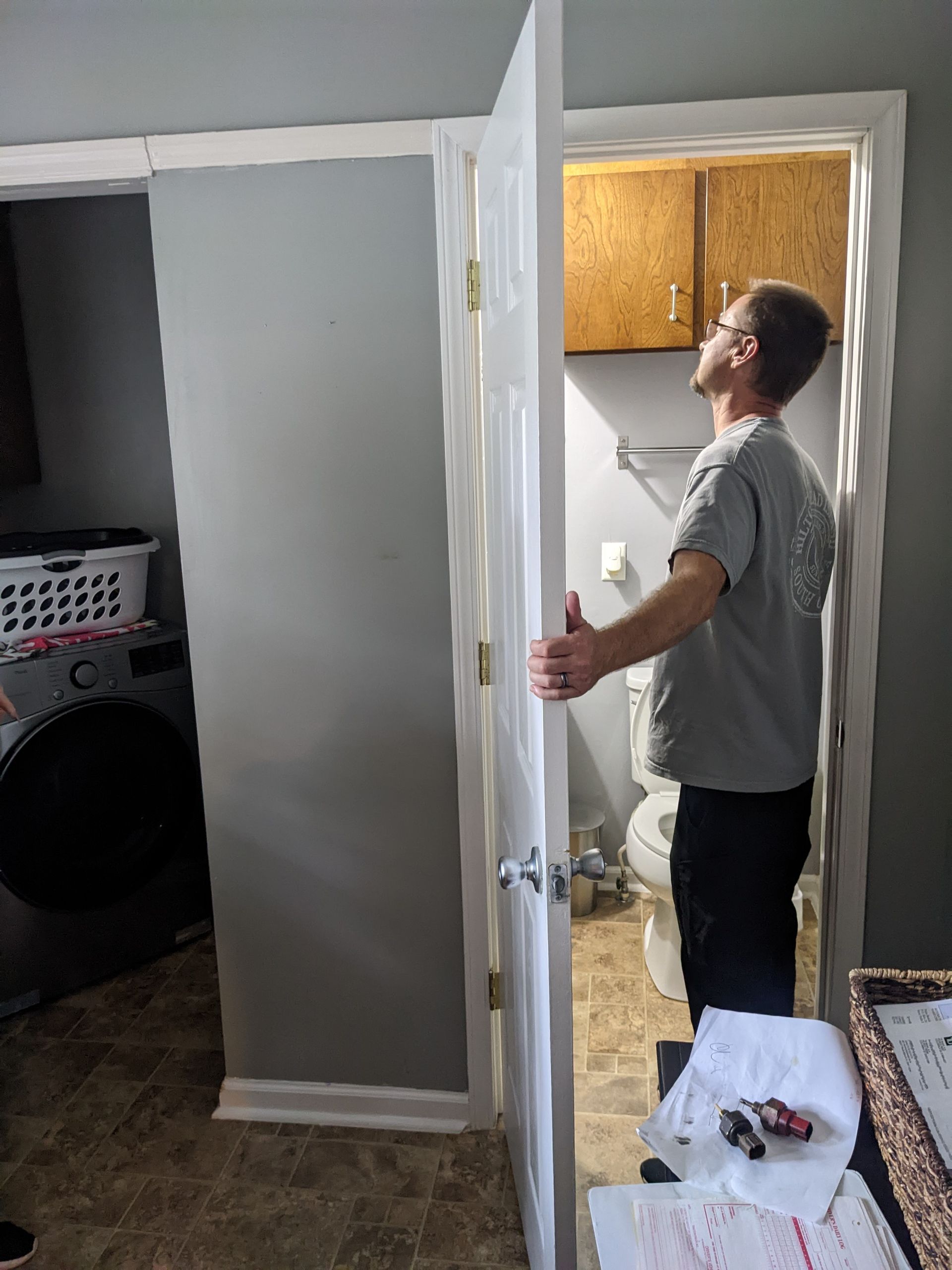 A man is standing in a bathroom holding a door open.