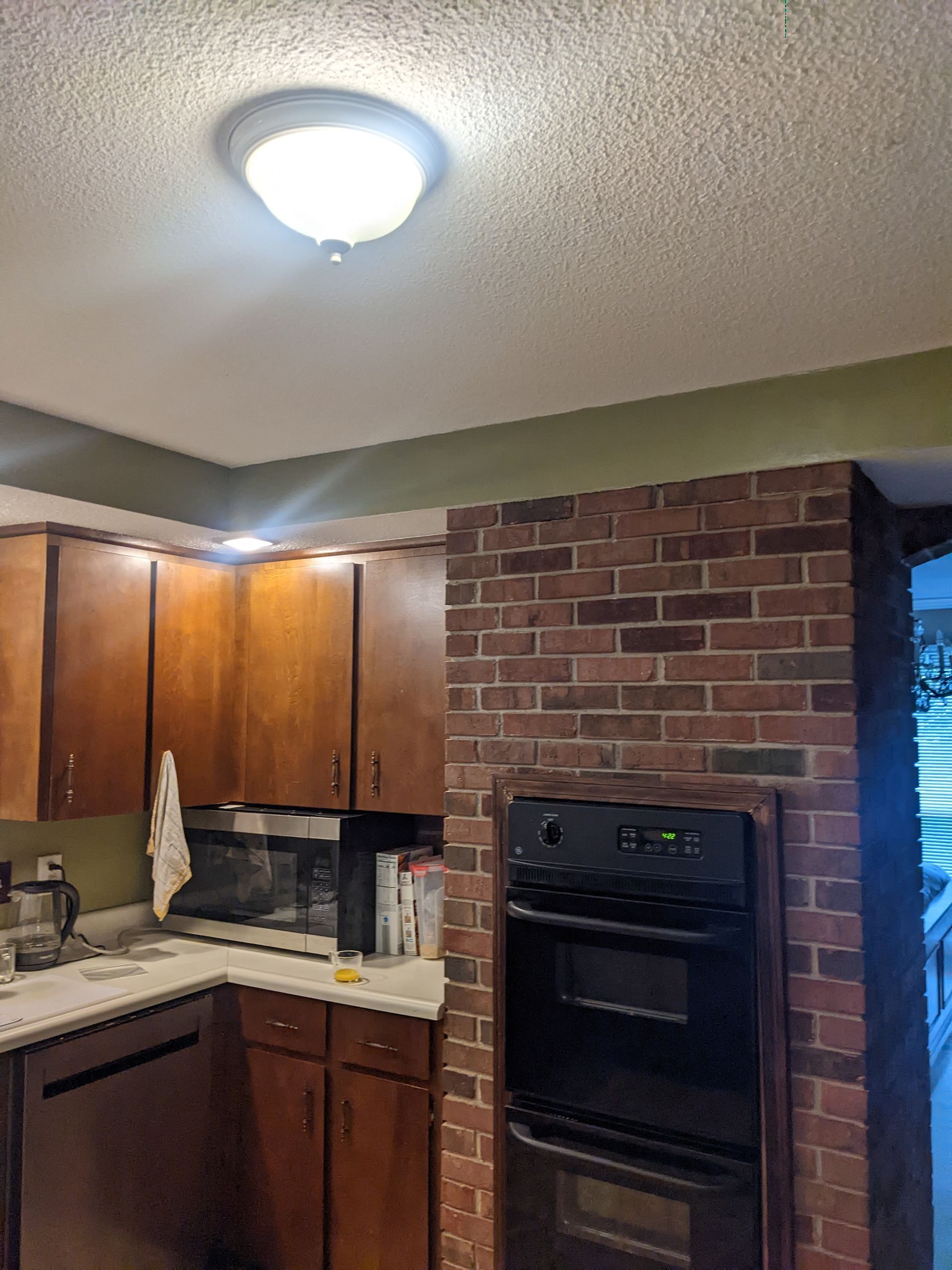 A kitchen with wooden cabinets , a stove , a microwave , and a brick wall.