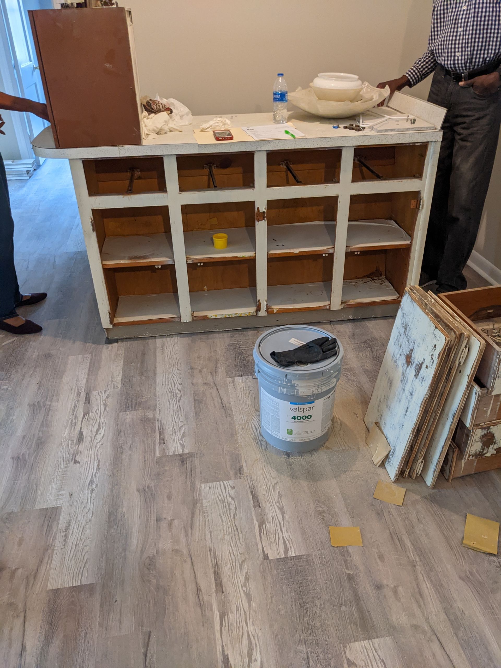 A dresser is being painted in a room with a bucket of paint on the floor.