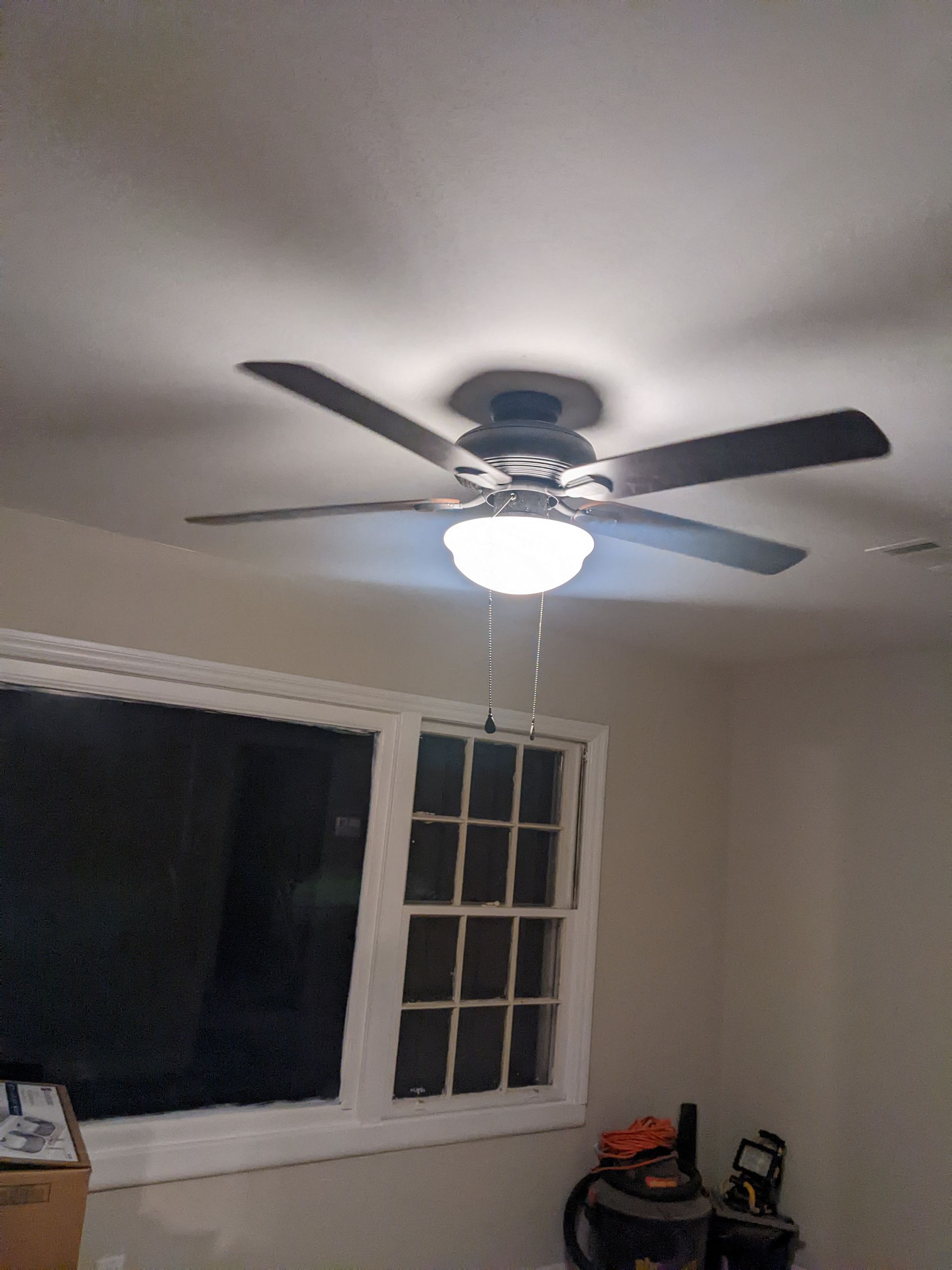 A ceiling fan is hanging from the ceiling in a room next to a window.