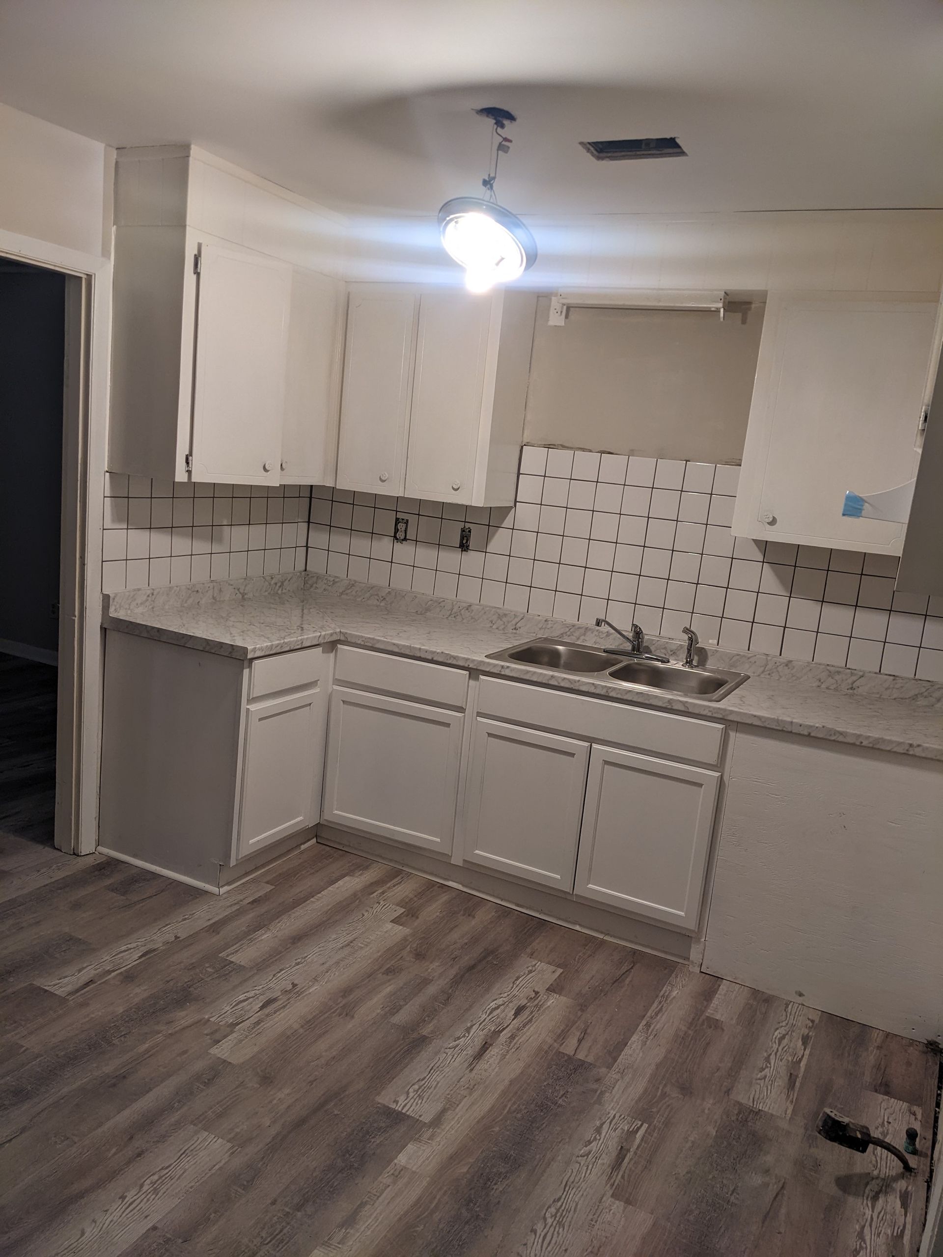 An empty kitchen with white cabinets and a sink.